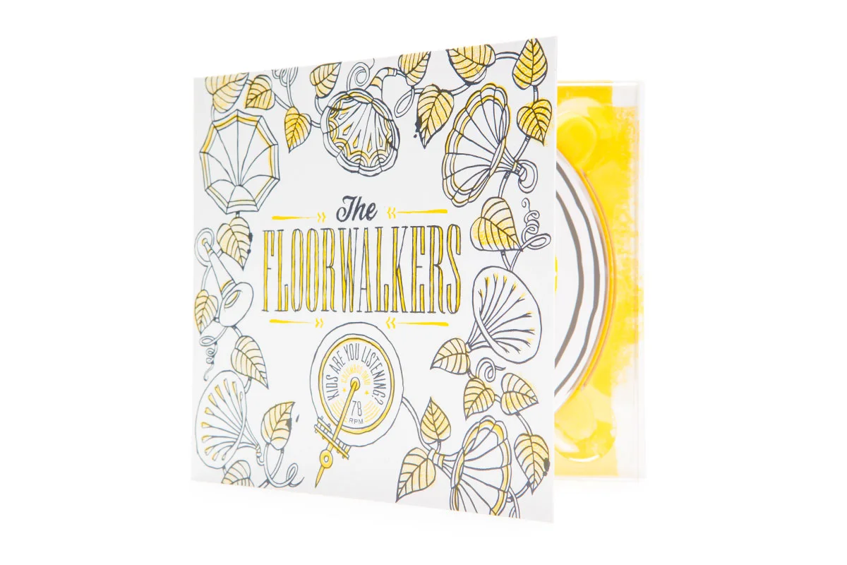 A decorative card with illustrations of leaves, umbrellas, mushrooms, and a gauge that says "Are you listening?" with a needle pointing to 78 RPM. Partially visible behind the card is a glass of yellow-colored beverage with ice and lemon slices.
