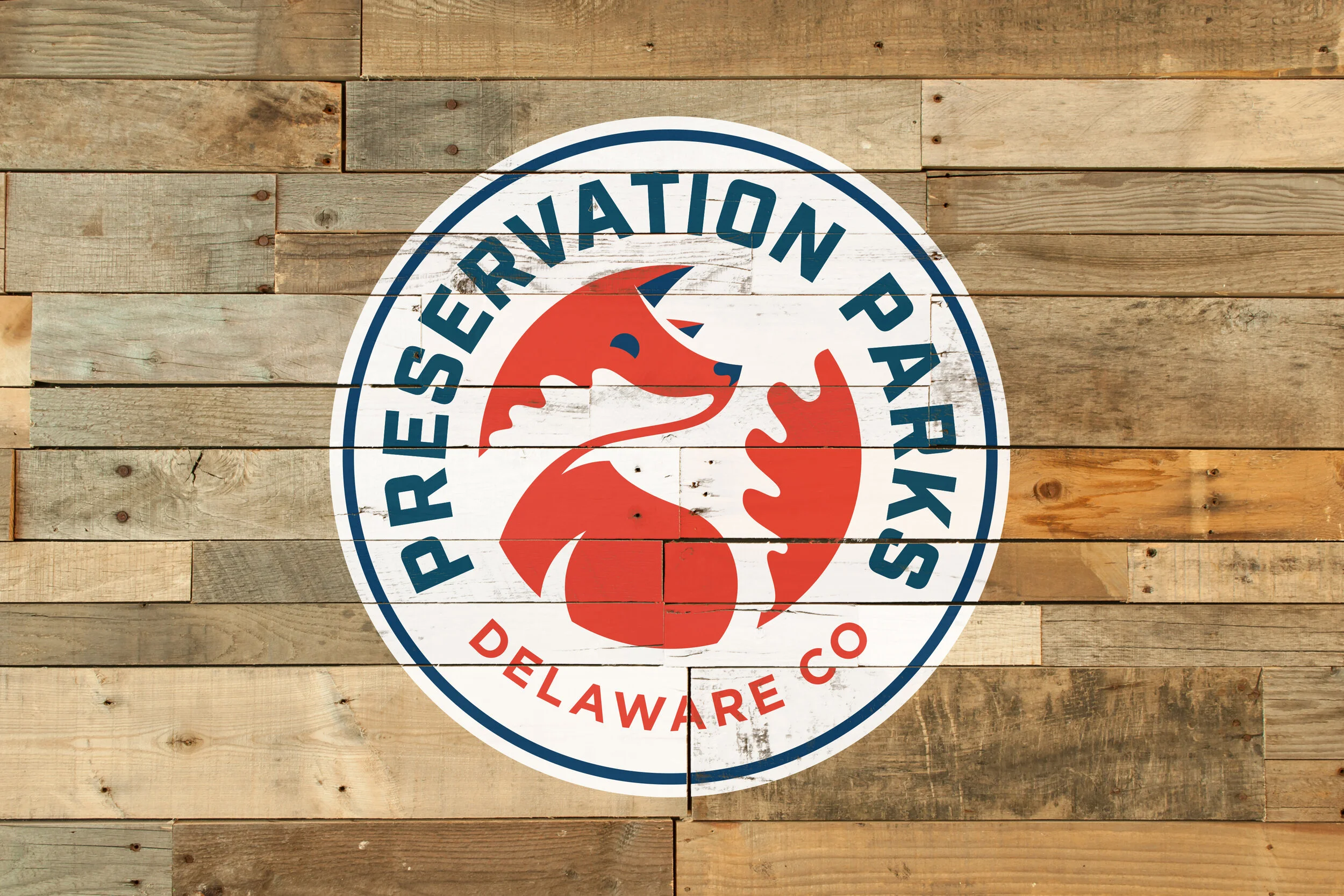 Circular logo of the Preservation Park in Delaware Co, with a stylized fox and a hand, on a wooden background.