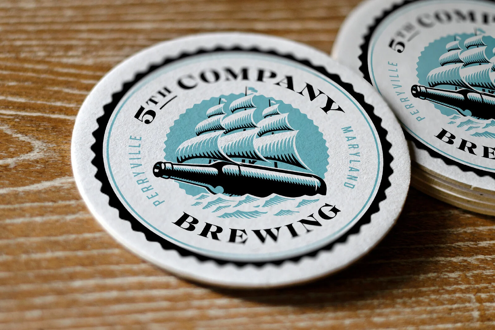 Round coasters with a vintage-style logo of a sailing ship and a pen, reading "5th Company," "Brewery," and "Marland," on a wooden surface.