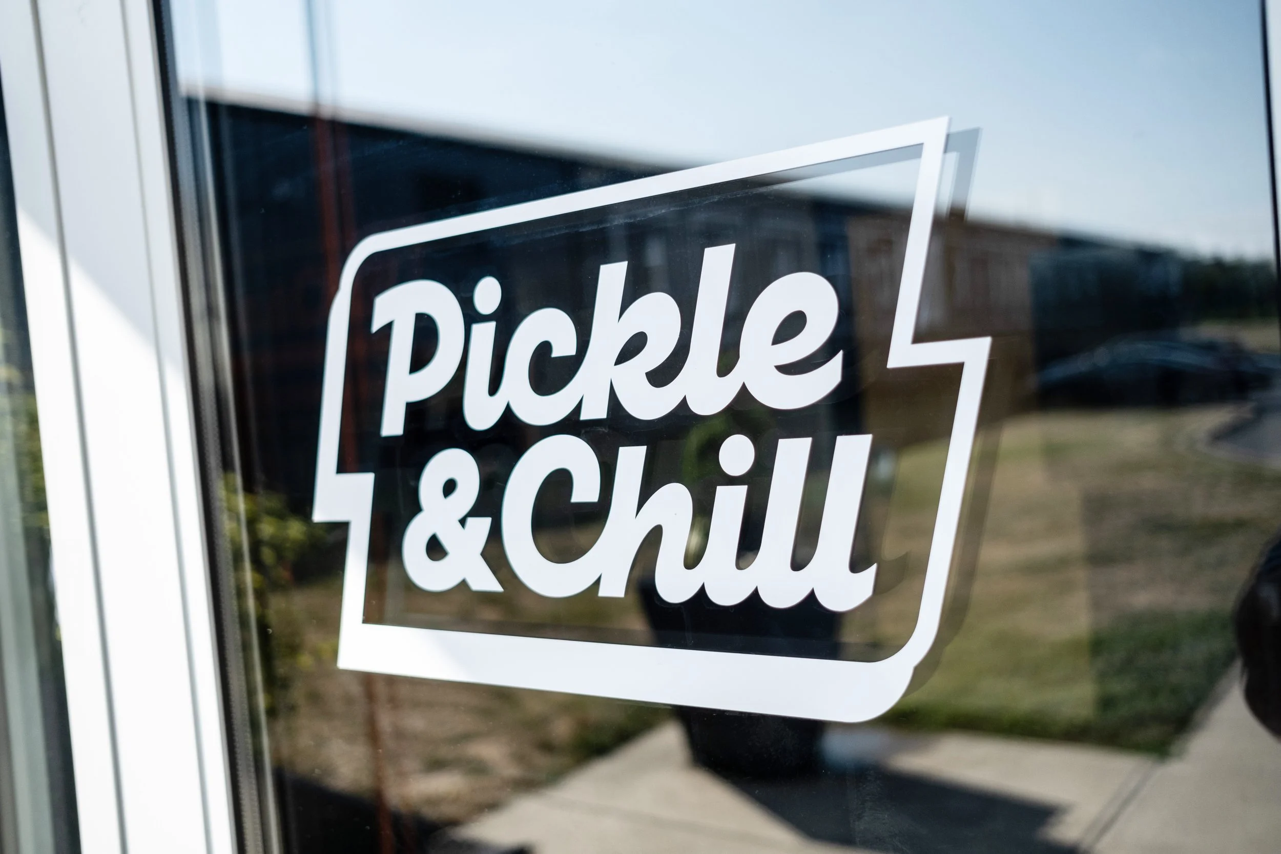 Pickle & Chill Indoor Pickleball Sign on a window that reads 'Pickle & Chill' in white text with a modern font.