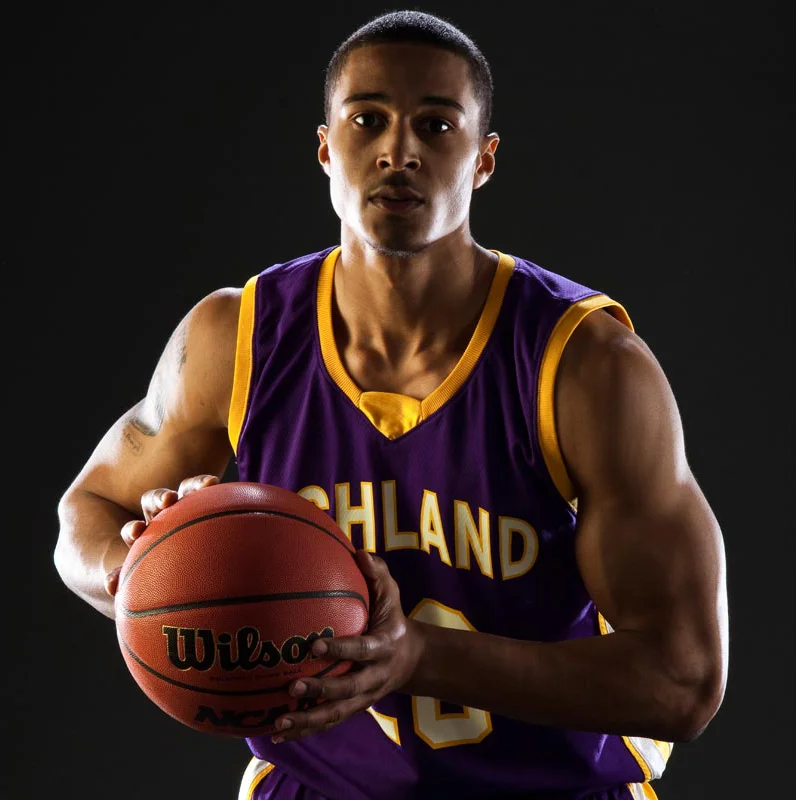 Young male basketball player in a purple and yellow jersey holding a basketball.