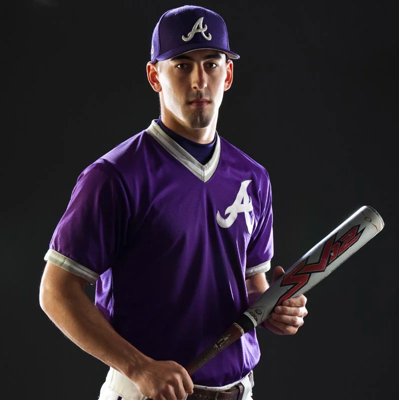 A young man wearing a baseball uniform with a purple jersey and cap, holding a baseball bat.