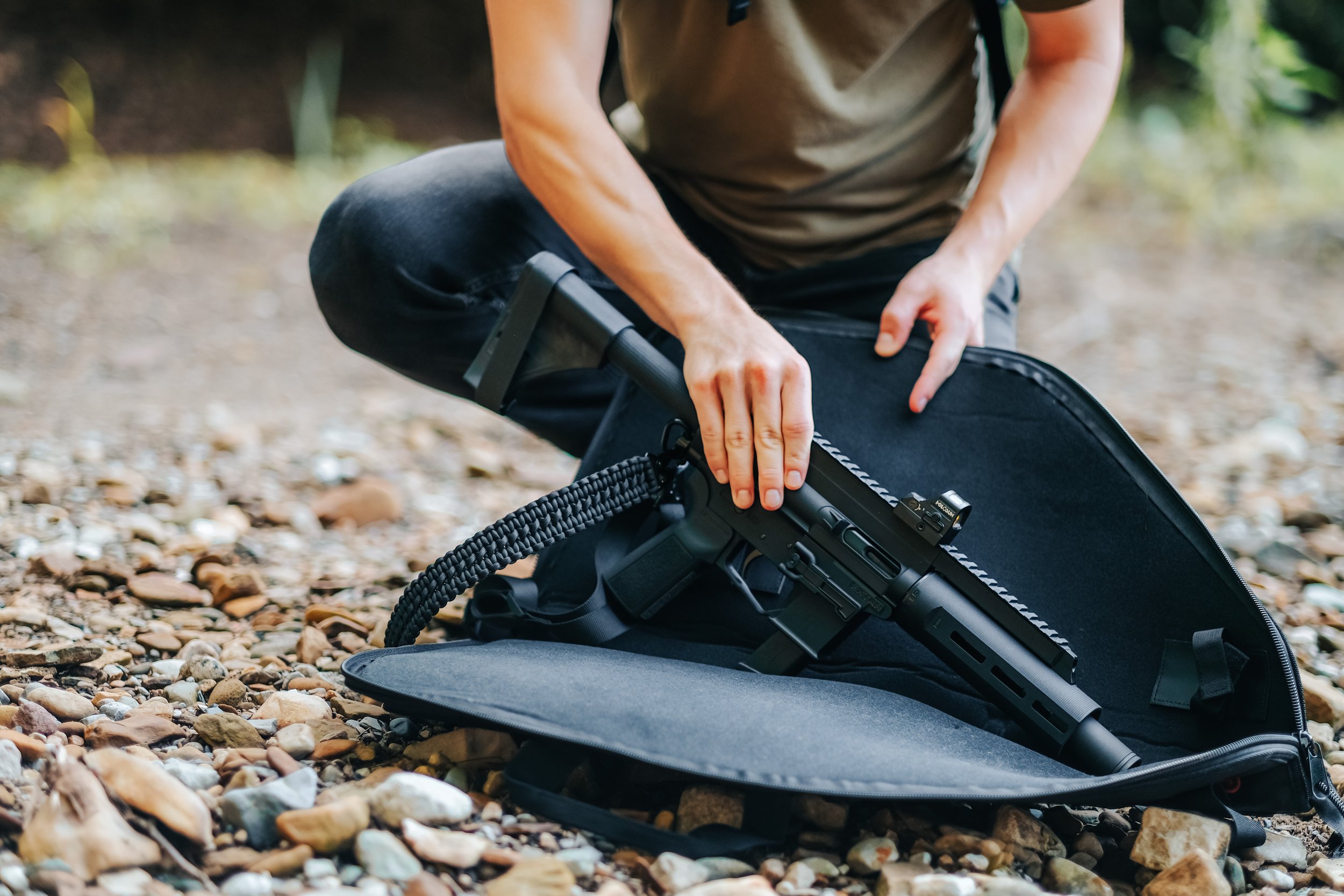 Person retrieving a firearm from a black soft case on a rocky ground.