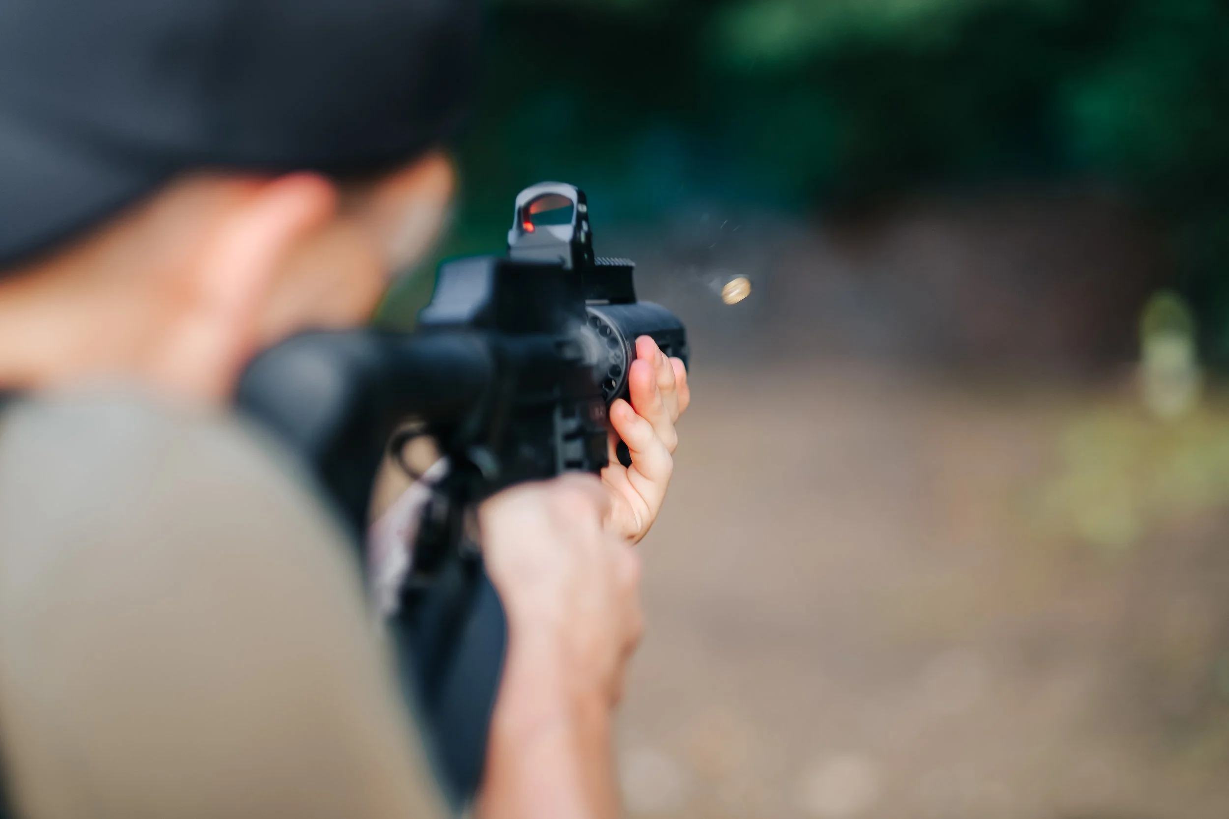 Person aiming a handgun with an illuminated red dot sight in an outdoor setting