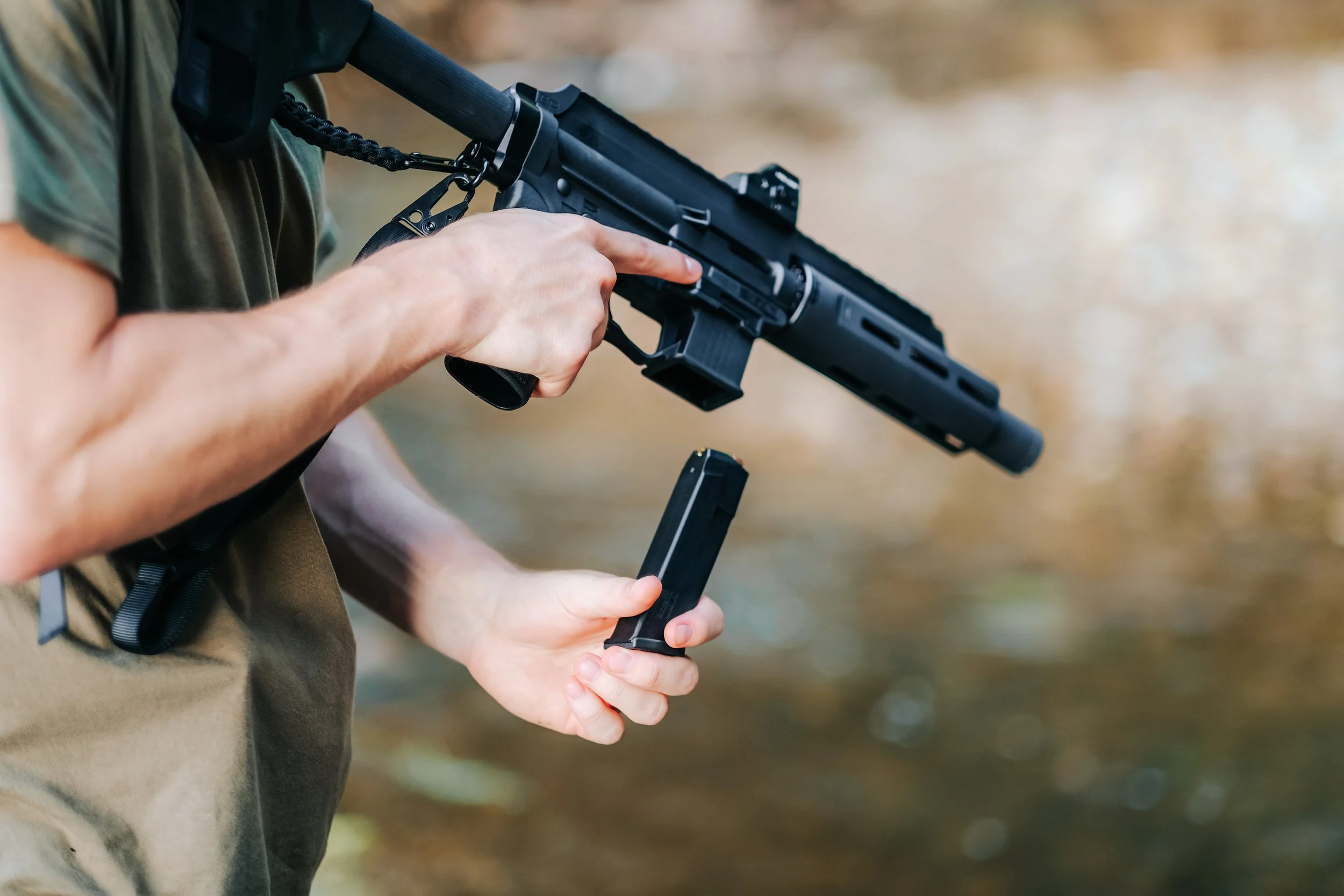 Person holding a semi-automatic rifle with a loaded magazine outside, with a blurred natural background.