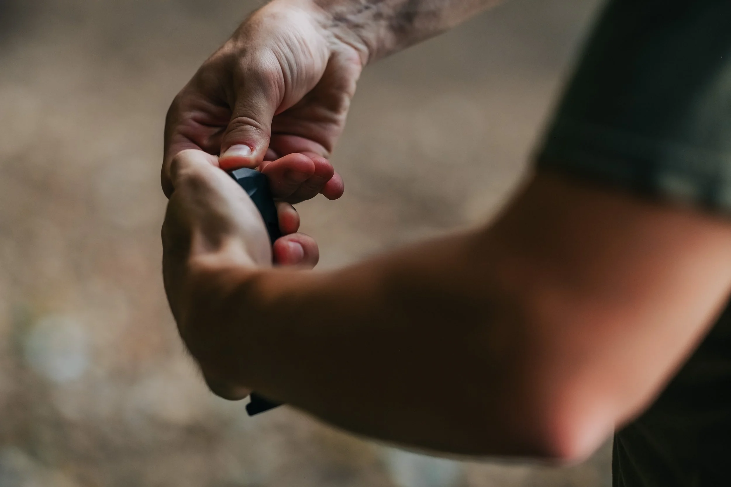 A person's hand with some hair is gripping and turning a small black and gray object, possibly a key, against a blurred background.