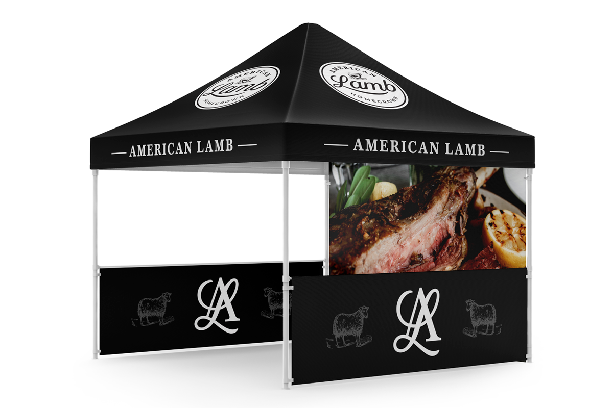 A black and white outdoor food tent with the words "American Lamb" and a logo, featuring a large image of cooked lamb with lemon and herbs on the side.