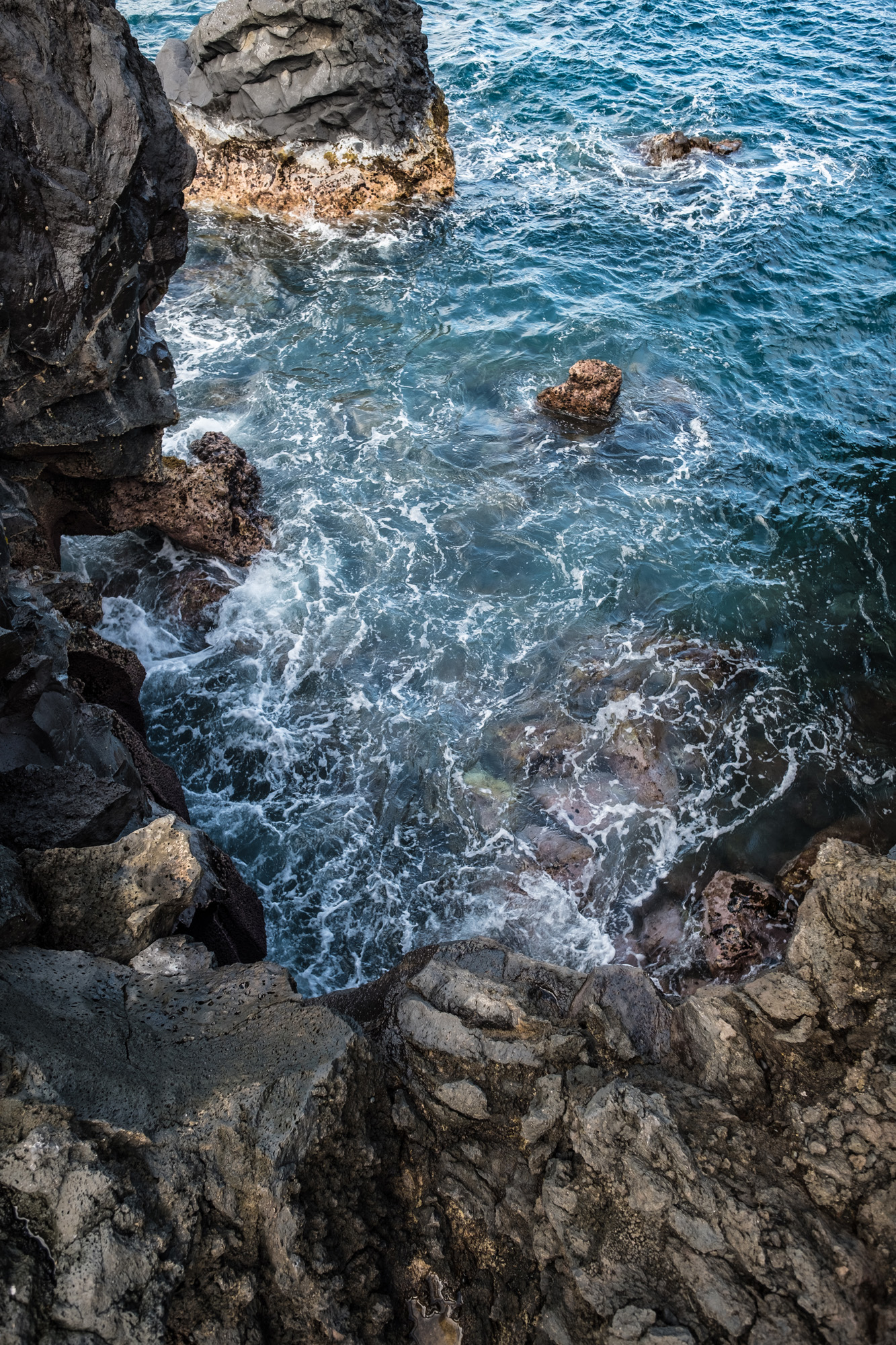 Rocky shoreline with dark volcanic rocks and ocean waves crashing against them in Maui.