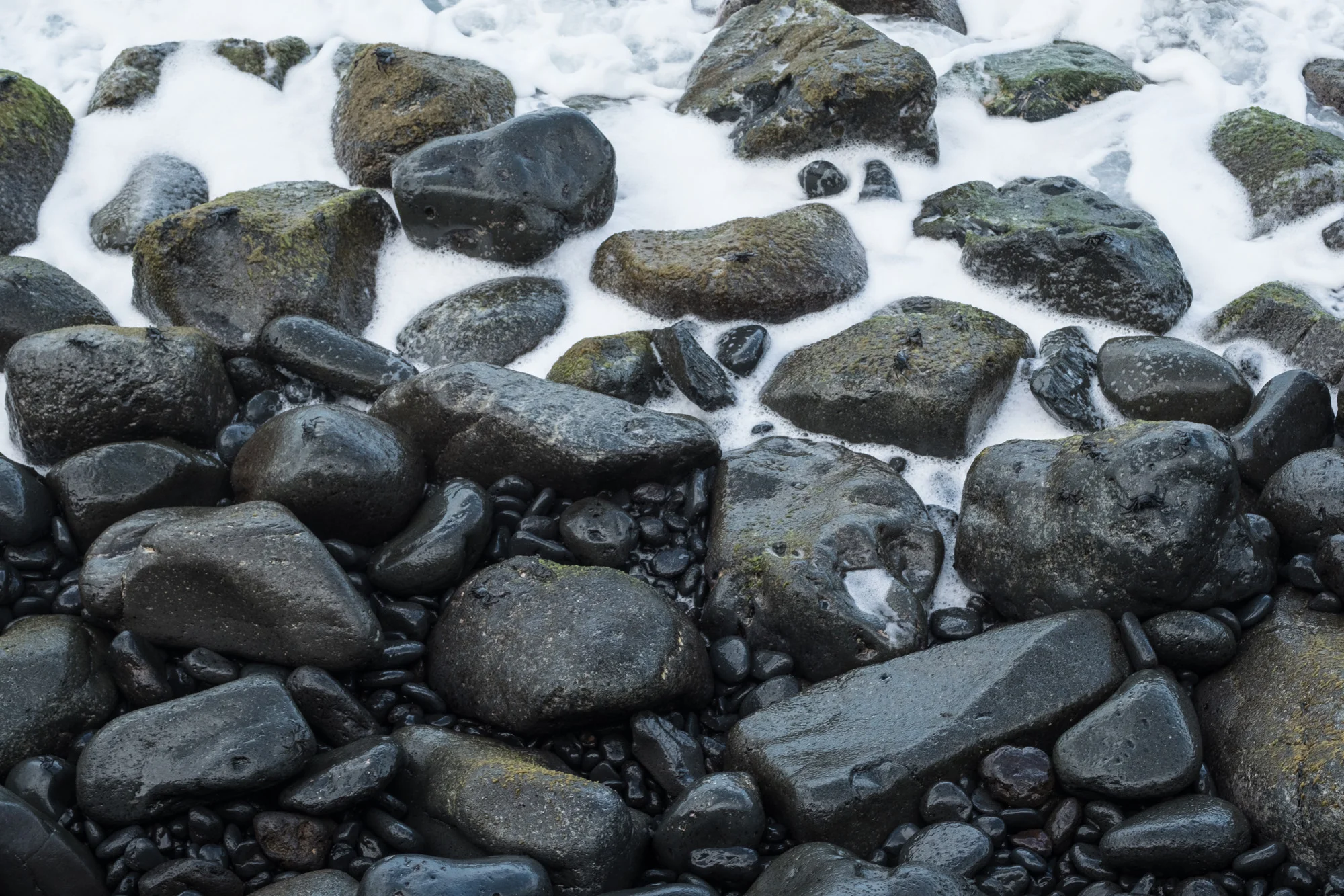 Rocks and pebbles on a beach with water flowing over them in Maui.