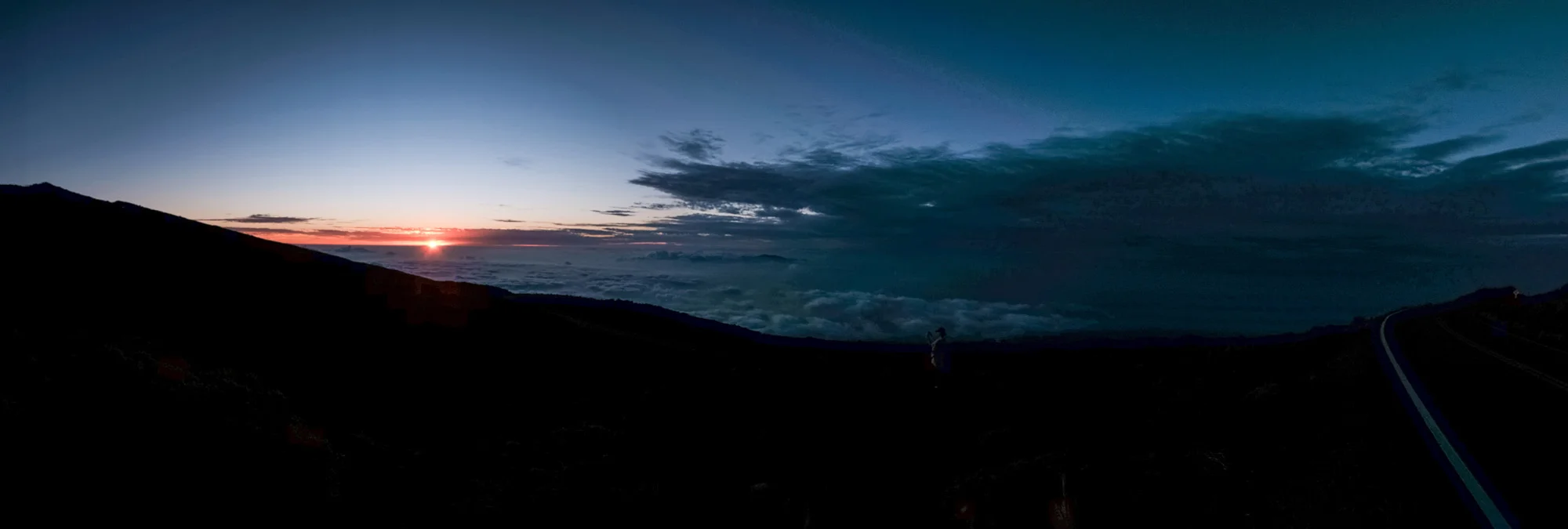 Sunset over a mountain with clouds in the sky and a person standing on the ground Maui.