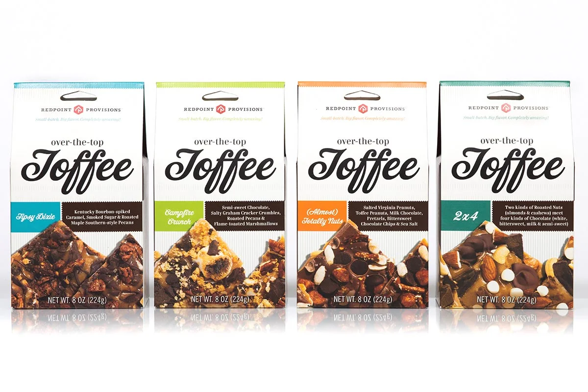 Four boxes of Redpoint Provisions over-the-top toffee with different flavors, including Tippy Dixie, Campfire Crunch, Almost Salty Nuts, and 2x4, arranged in a row on a white background.