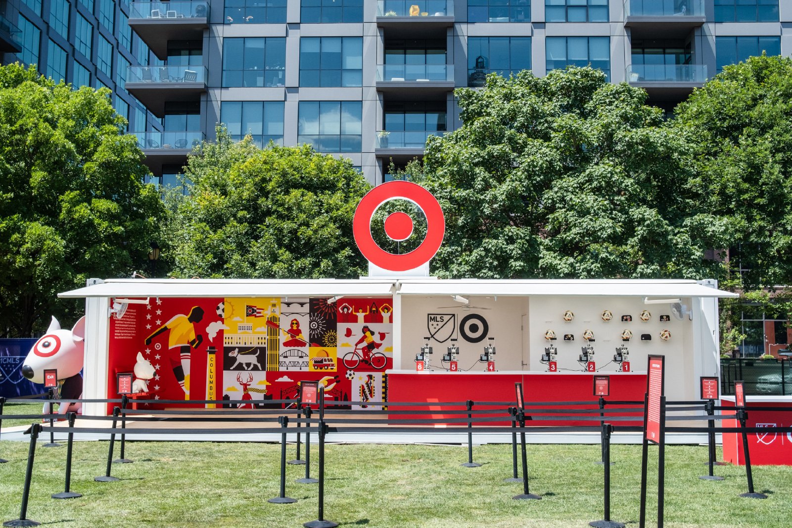 An outdoor display promoting Target with the Target logo on top. The display has a colorful mural featuring local symbols, including a person, a dog, a basketball player, and fireworks. There are multiple prize microphones numbered 1 through 6, along