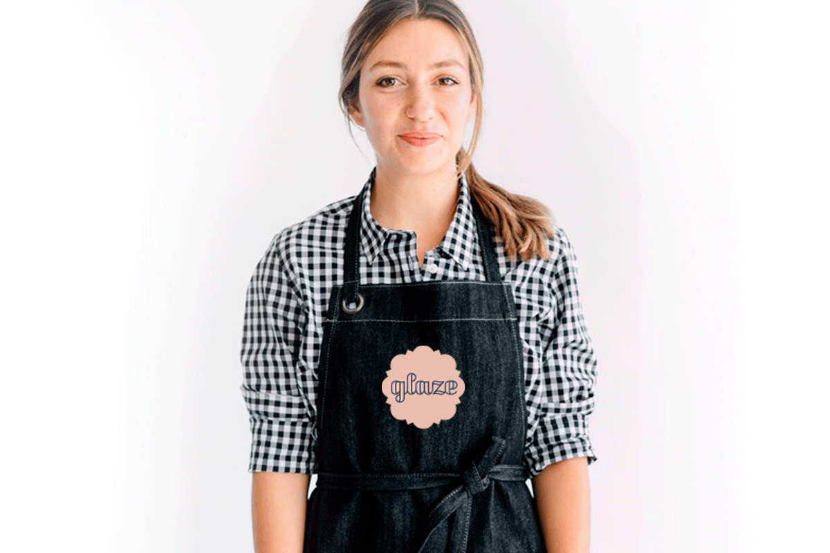 Young woman wearing a black apron with "glauze" printed on it, standing against a white background.