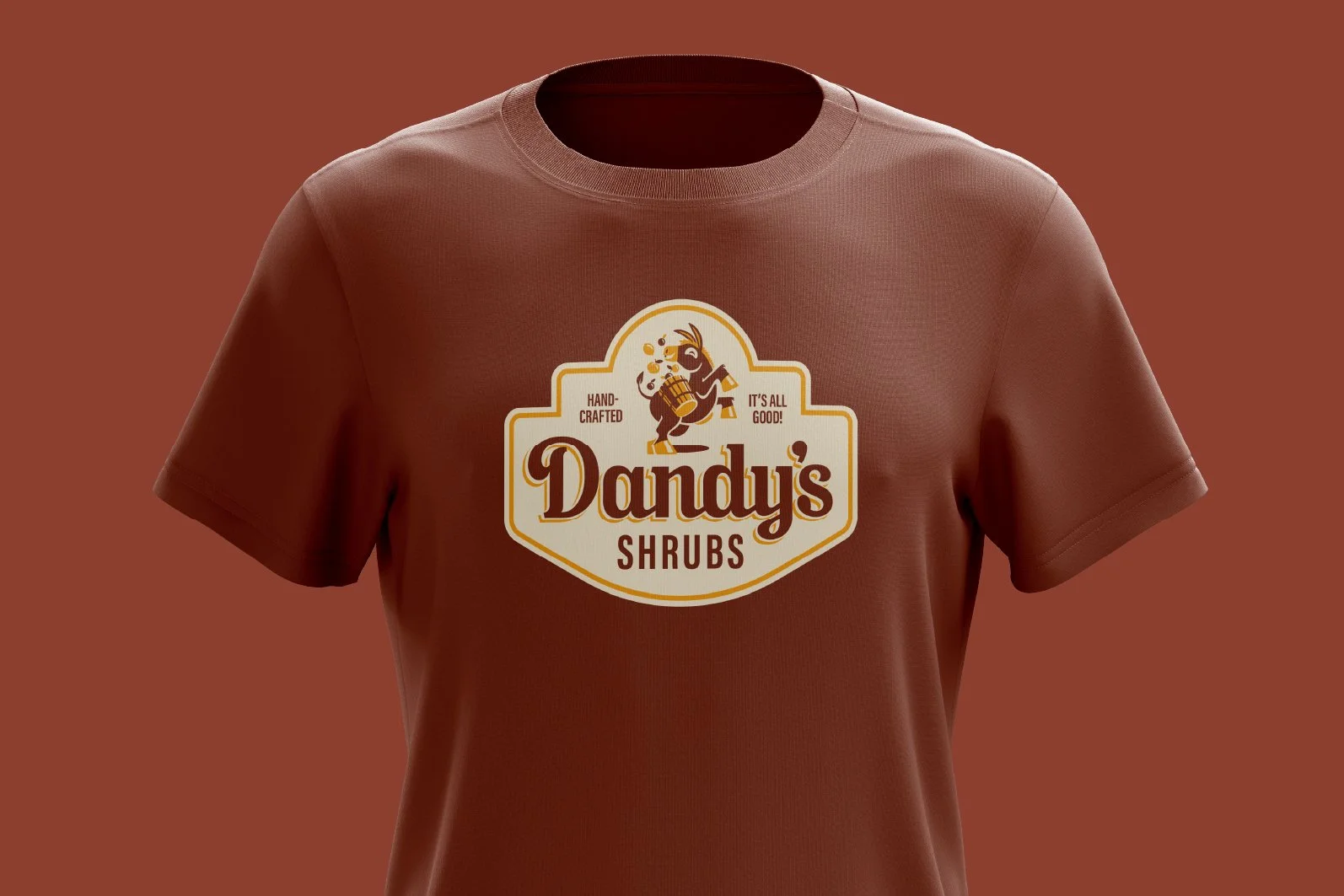 Brown t-shirt with a logo for Dandy's Shrubs featuring a cartoon deer holding a cup and a bottle, with the words "Hand Crafted" and "It's All Good!".
