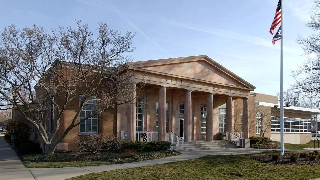 Front view of Ritter Library building with columns, trees, stairs, and an American flag in the foreground.