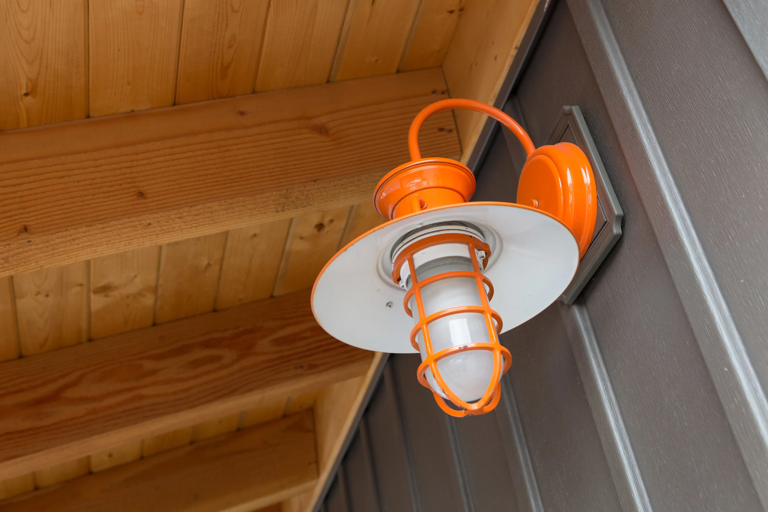 Orange and white birdhouse-shaped light fixture mounted on a wall with wooden ceiling above.