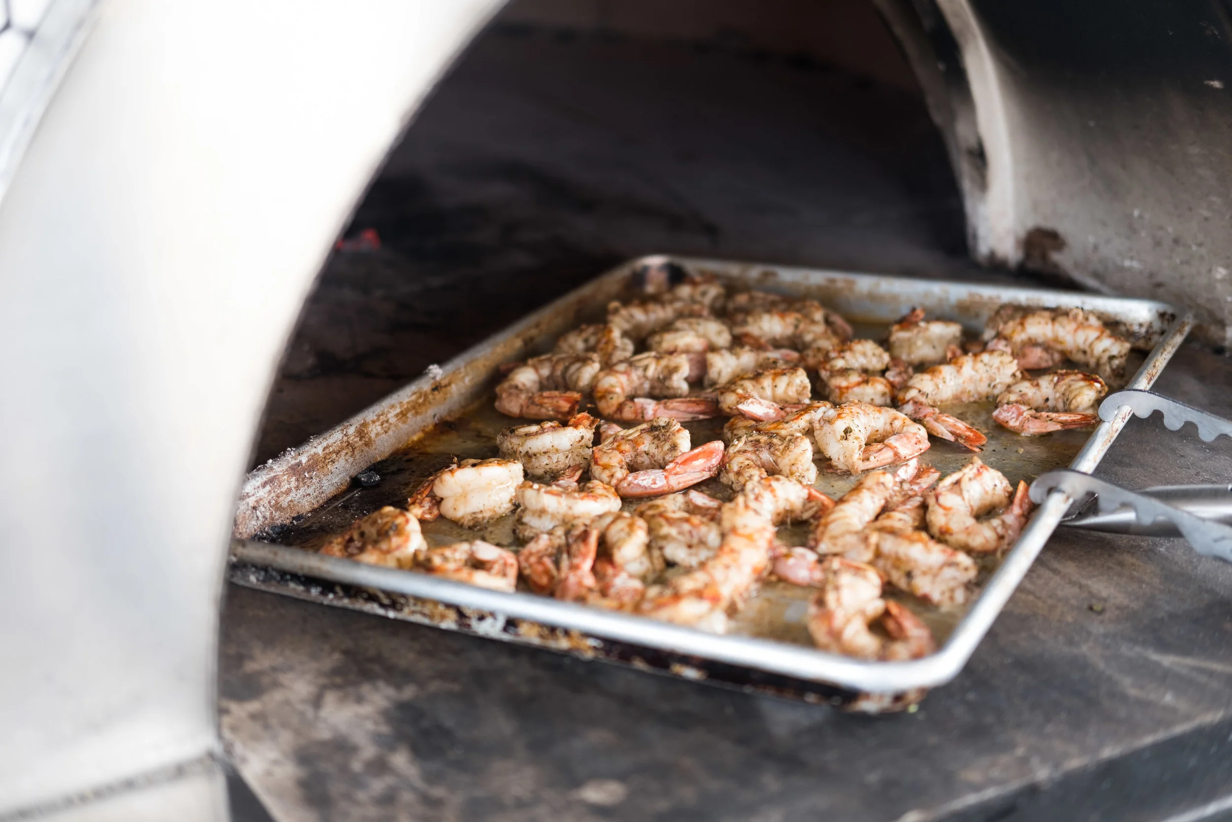 Shrimp being cooked on a tray inside an outdoor pizza oven.
