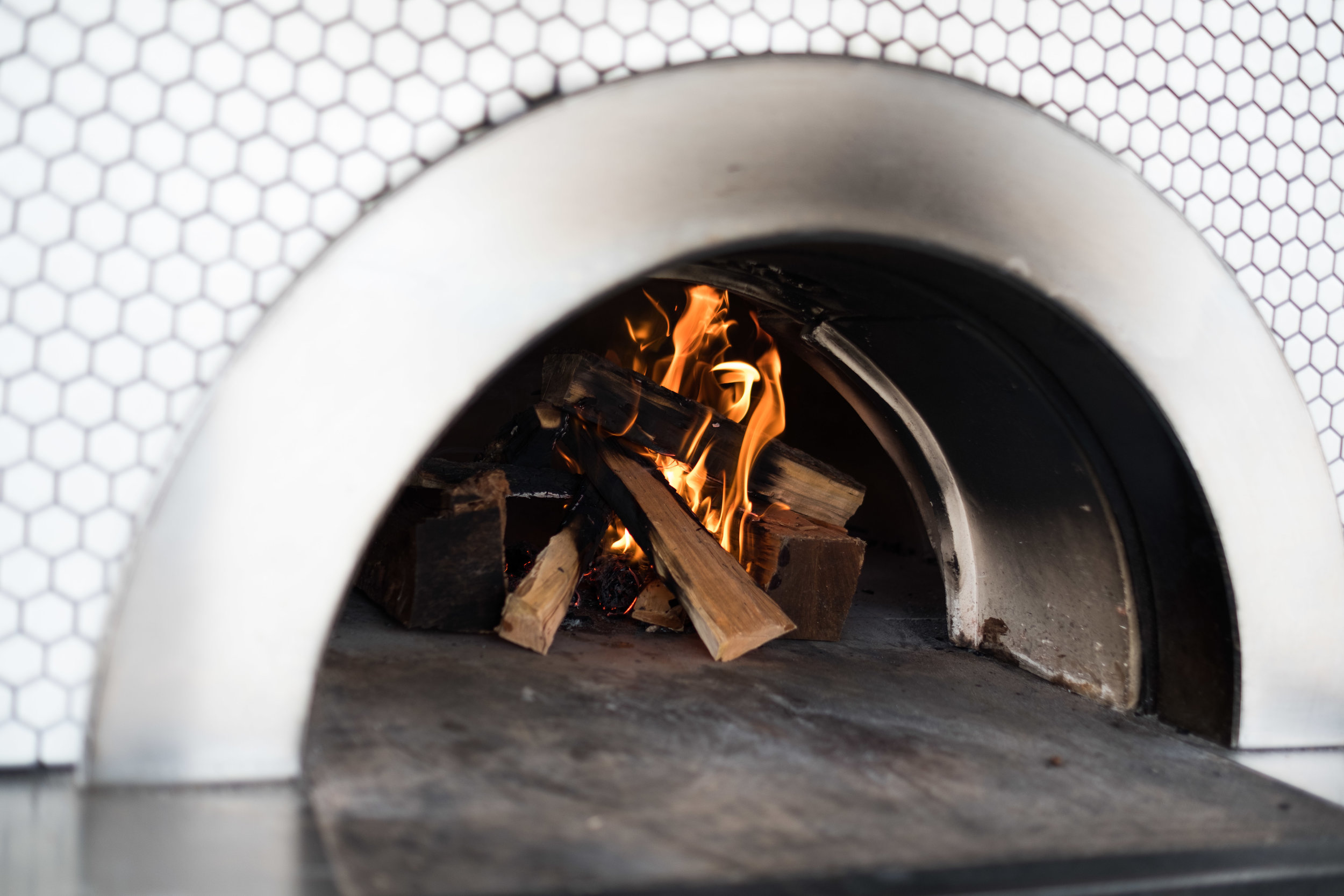 Inside a wood-fired oven with burning logs and flames, surrounded by a hexagon-patterned metal exterior.