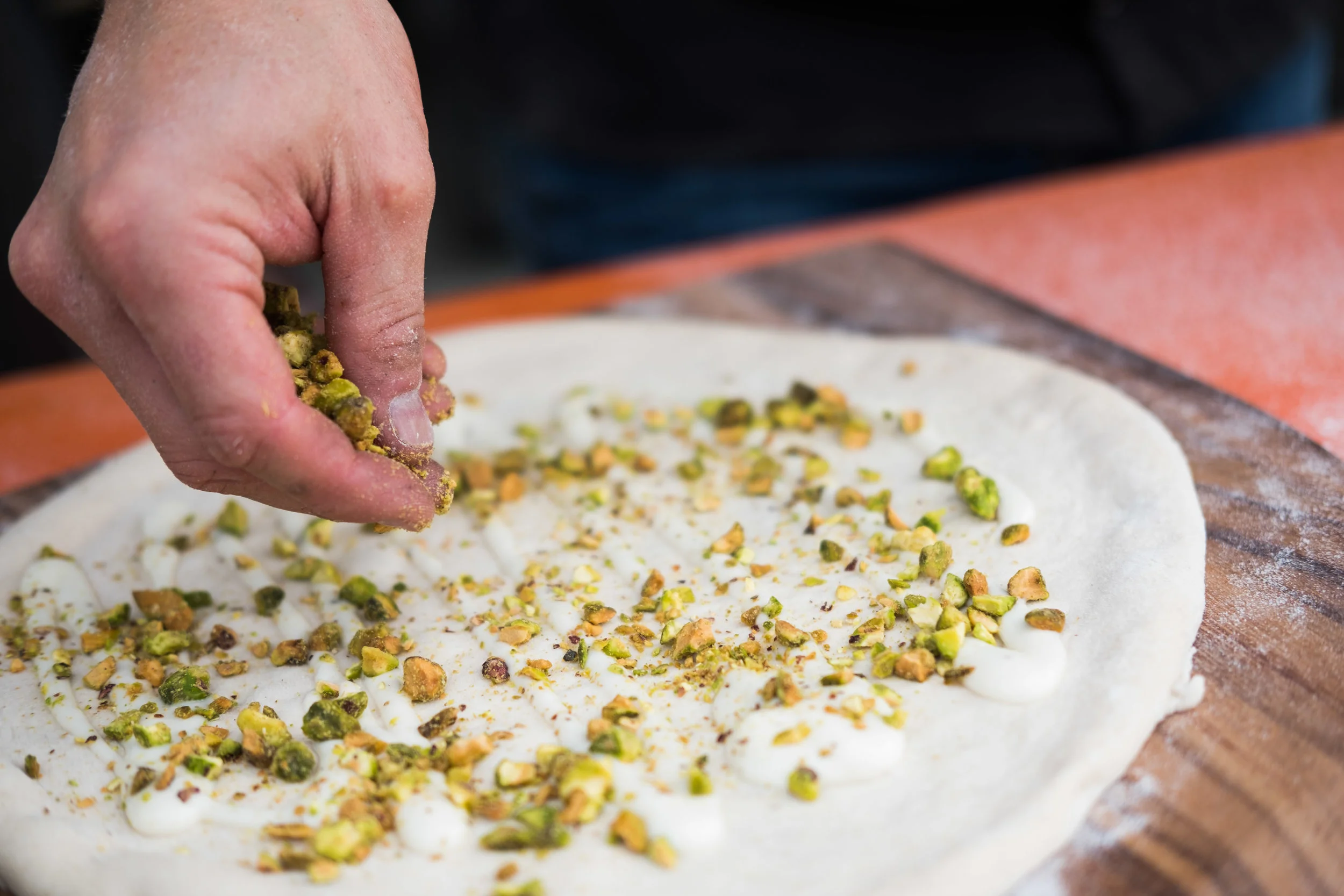 A person sprinkling chopped pistachios onto a rolled-out piece of dough in preparation for baking.