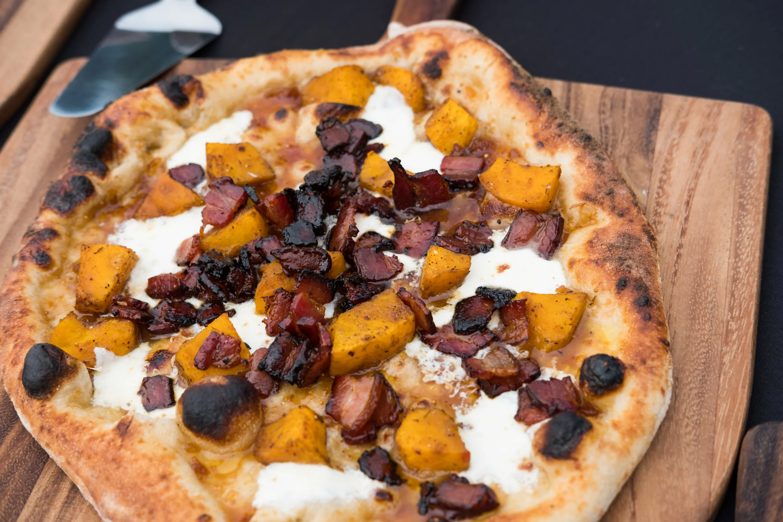 A pizza topped with roasted butternut squash, bacon, and cheese on a wooden board.