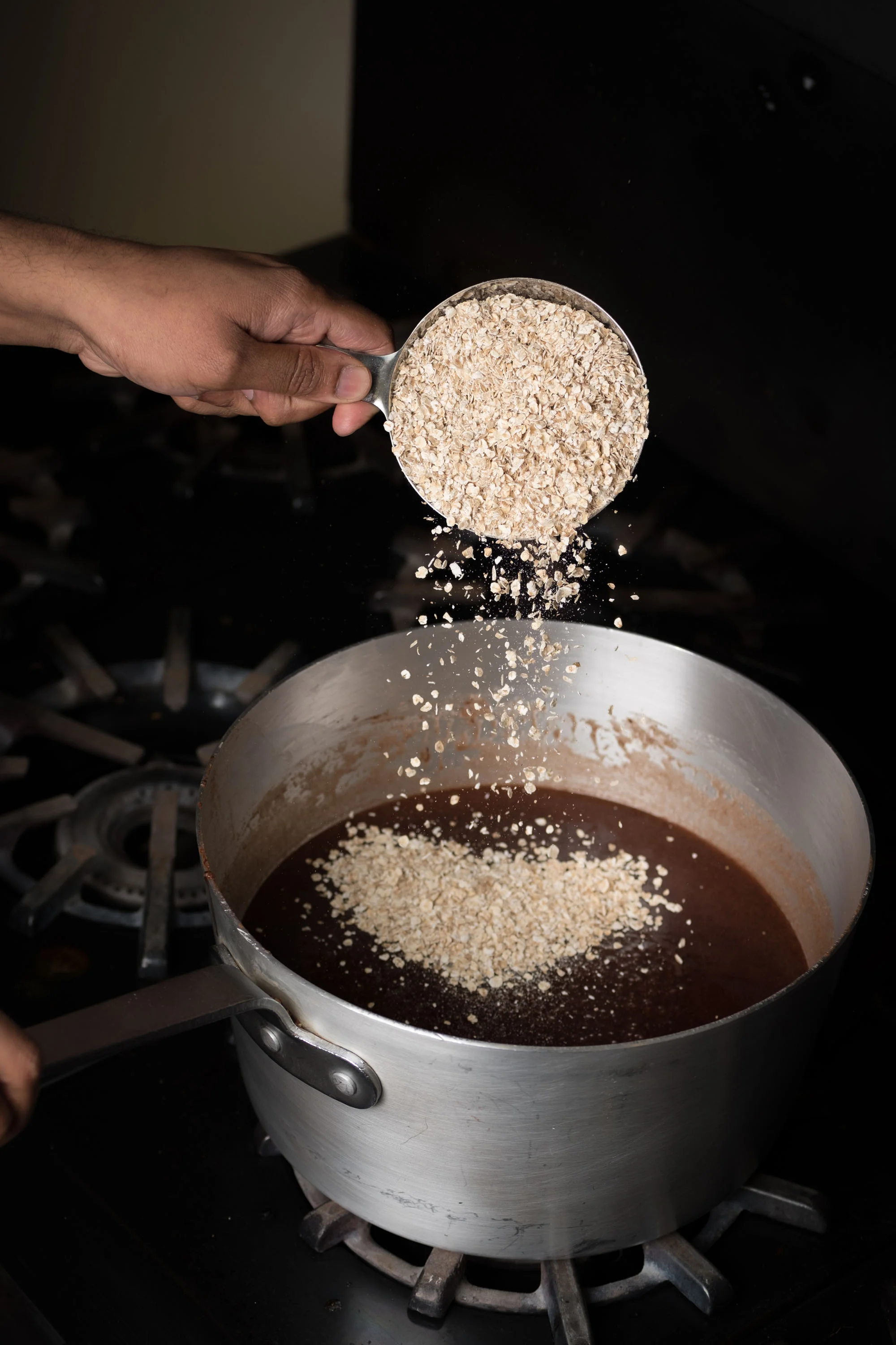 Person adding oats to a pot of chocolate mixture on a stove.
