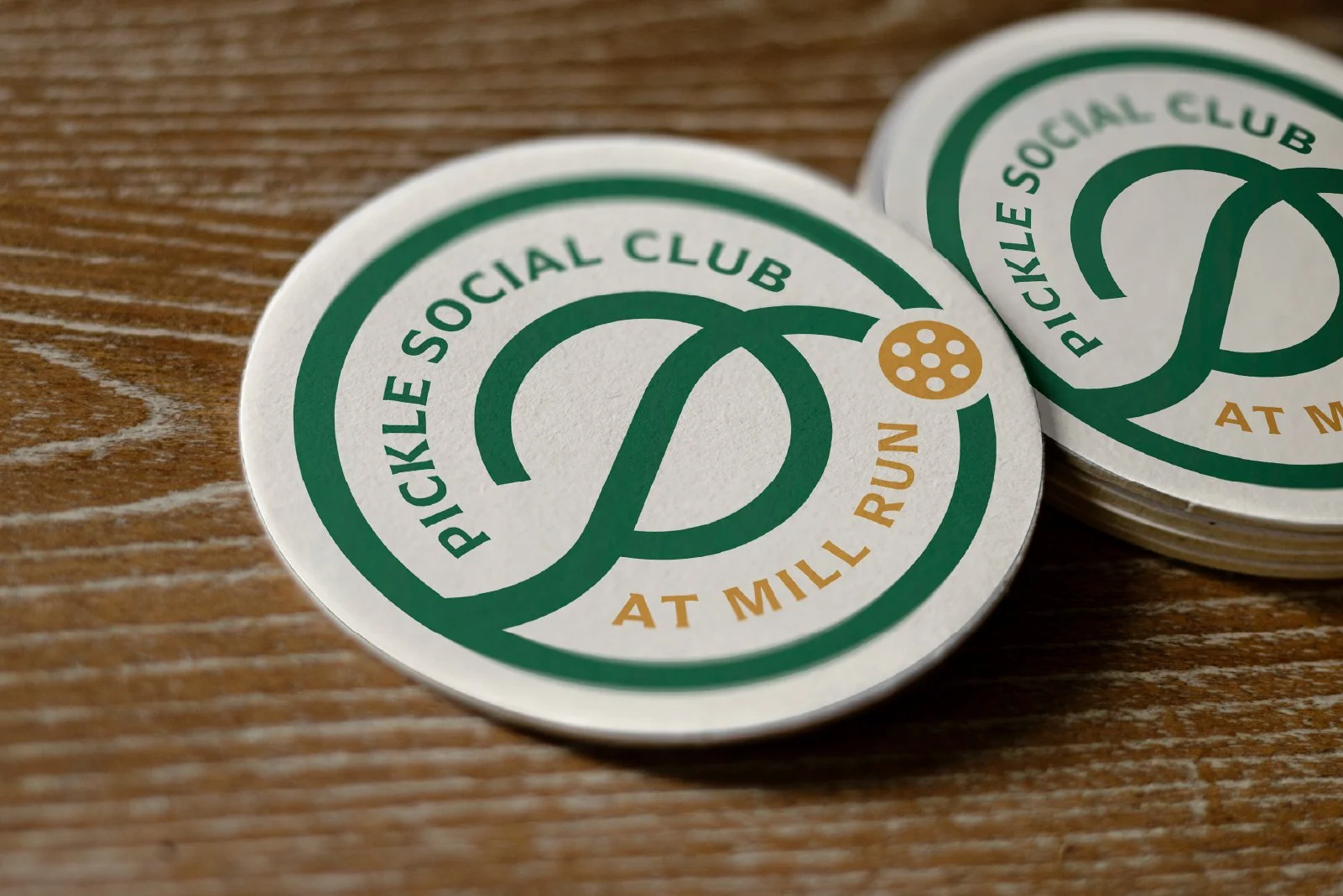 Round coasters with green and gold logo for Pickle Social Club on wooden surface.