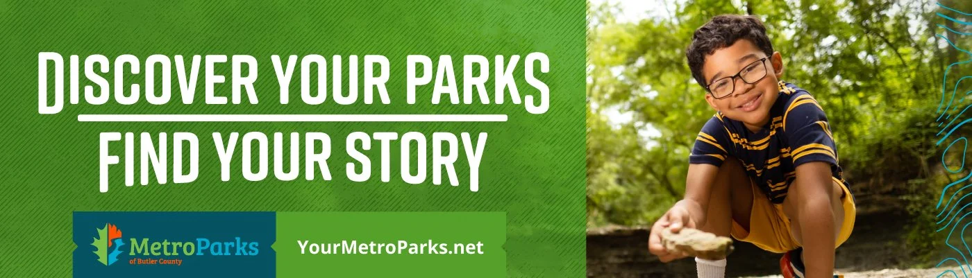 Young boy playing outdoors in a park, crouching down and smiling, with trees and greenery in the background, promoting discovering parks and outdoor stories.