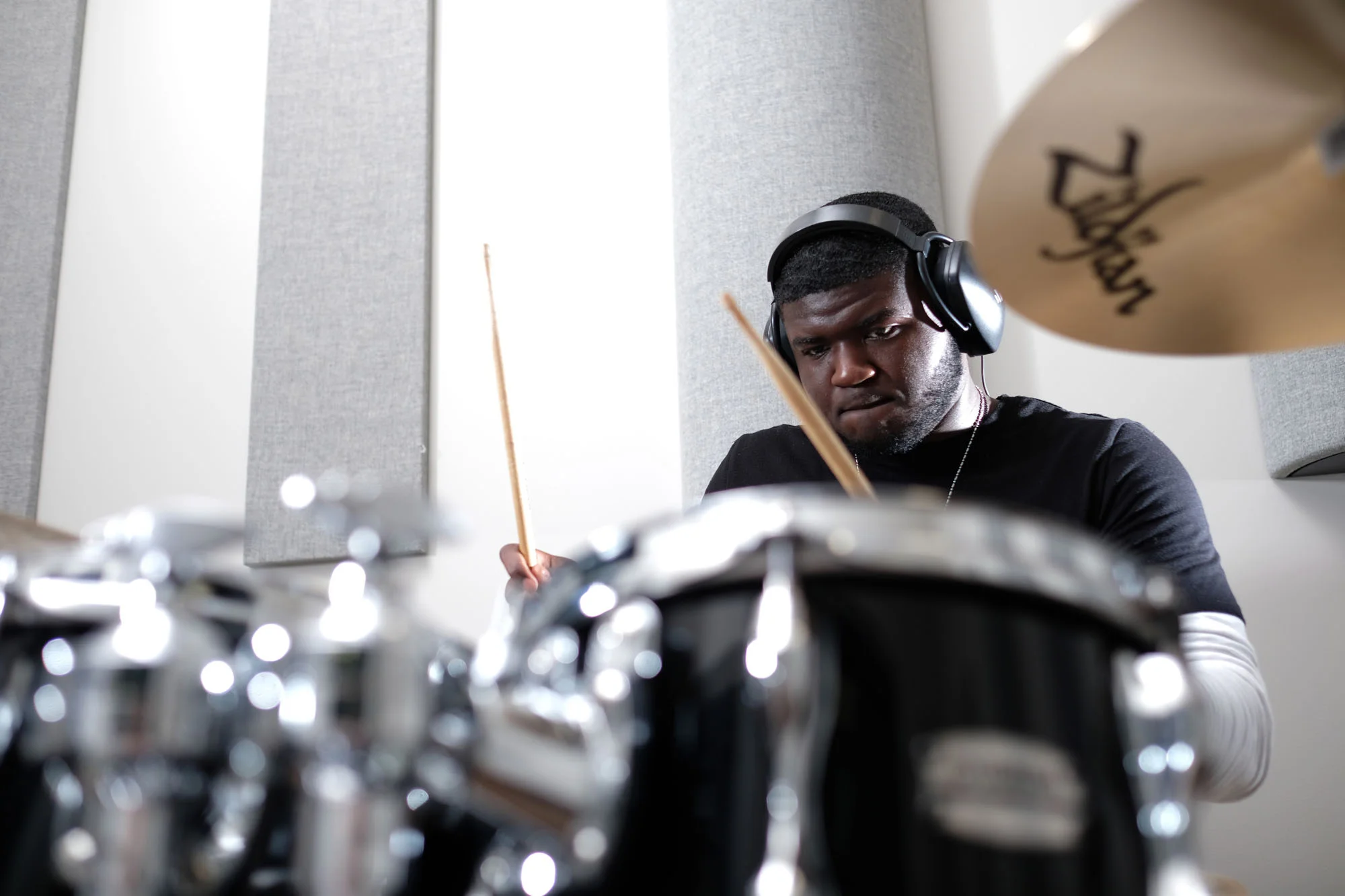A young man wearing headphones playing drums in a music studio.