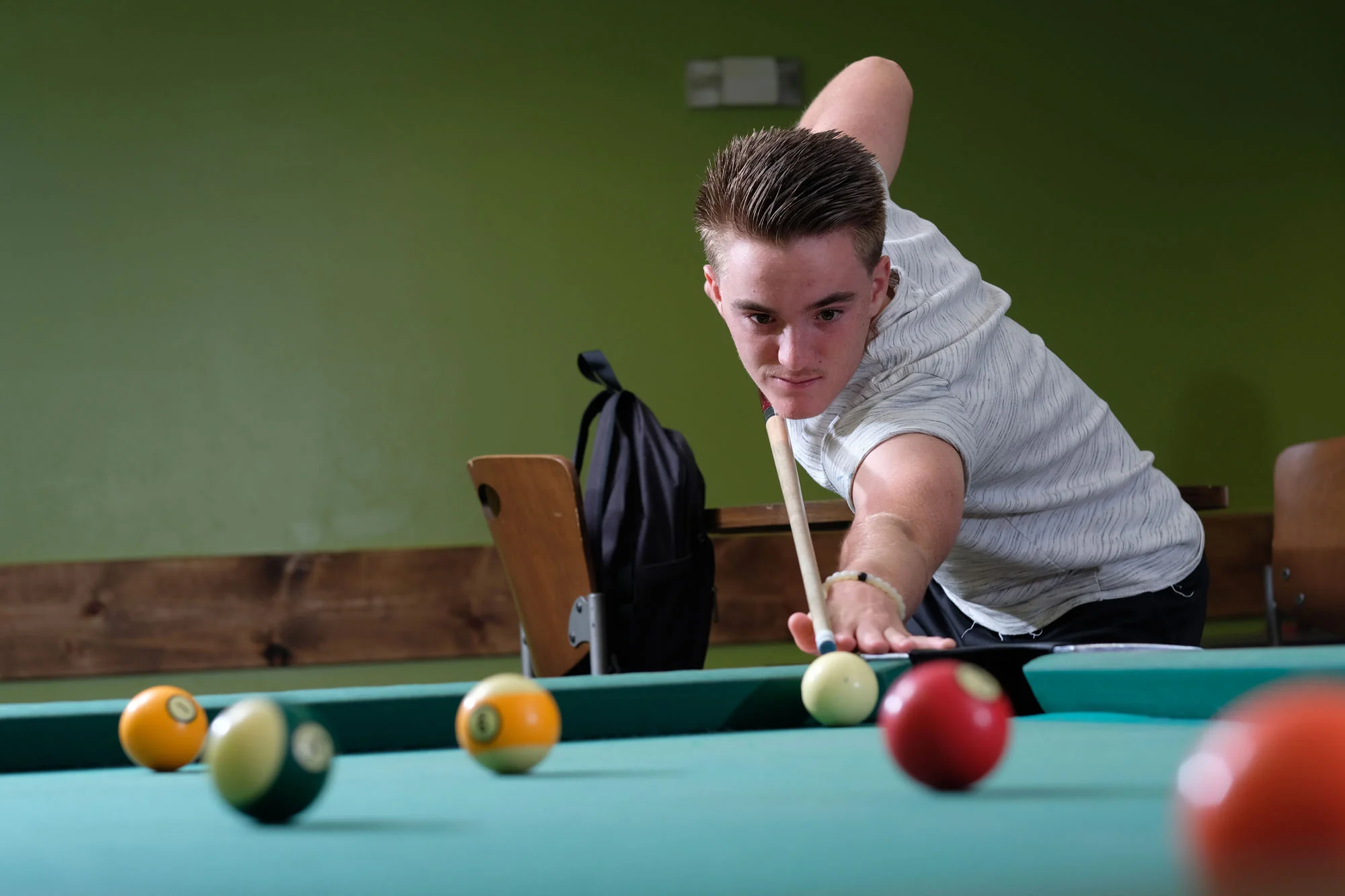 Young man playing billiards on a pool table, aiming to hit the cue ball.