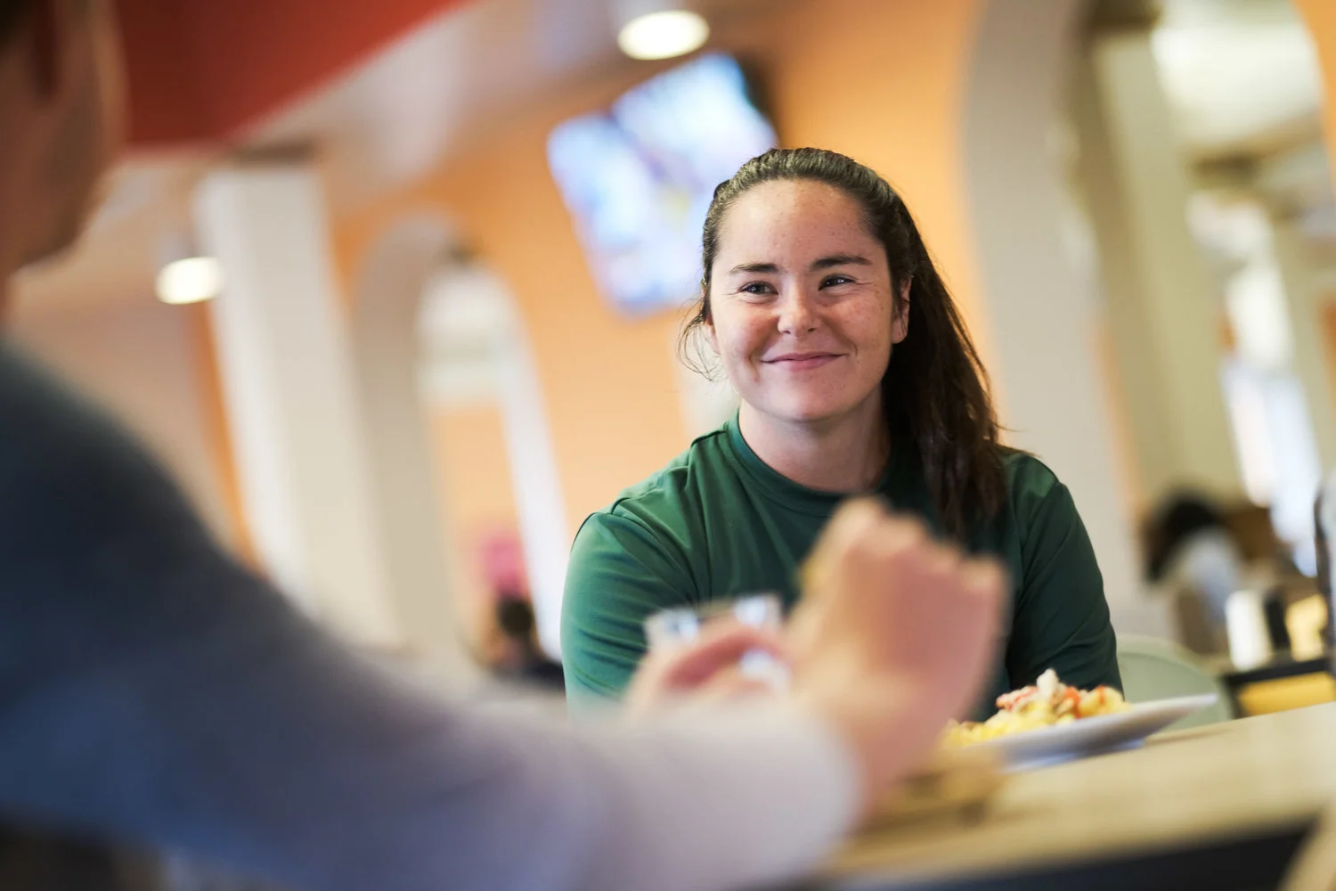 A woman smiling while talking to someone at a restaurant or café.