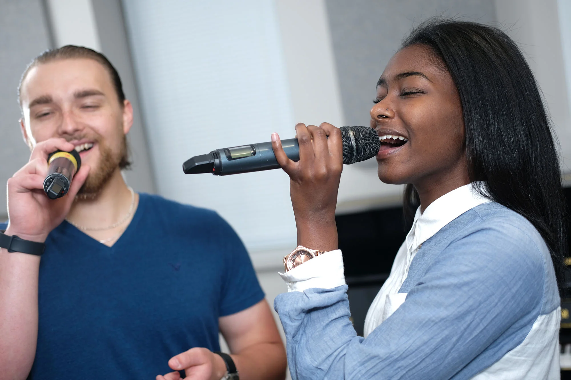 Two people singing into microphones, one woman and one man, in a music studio.