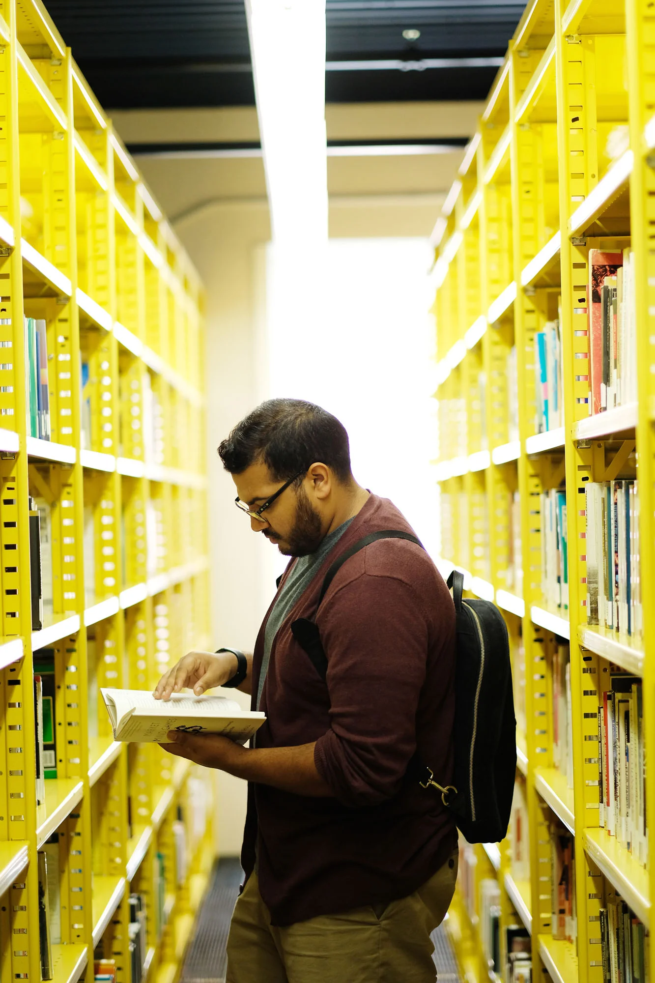 A man browsing books in a library aisle with yellow shelves.