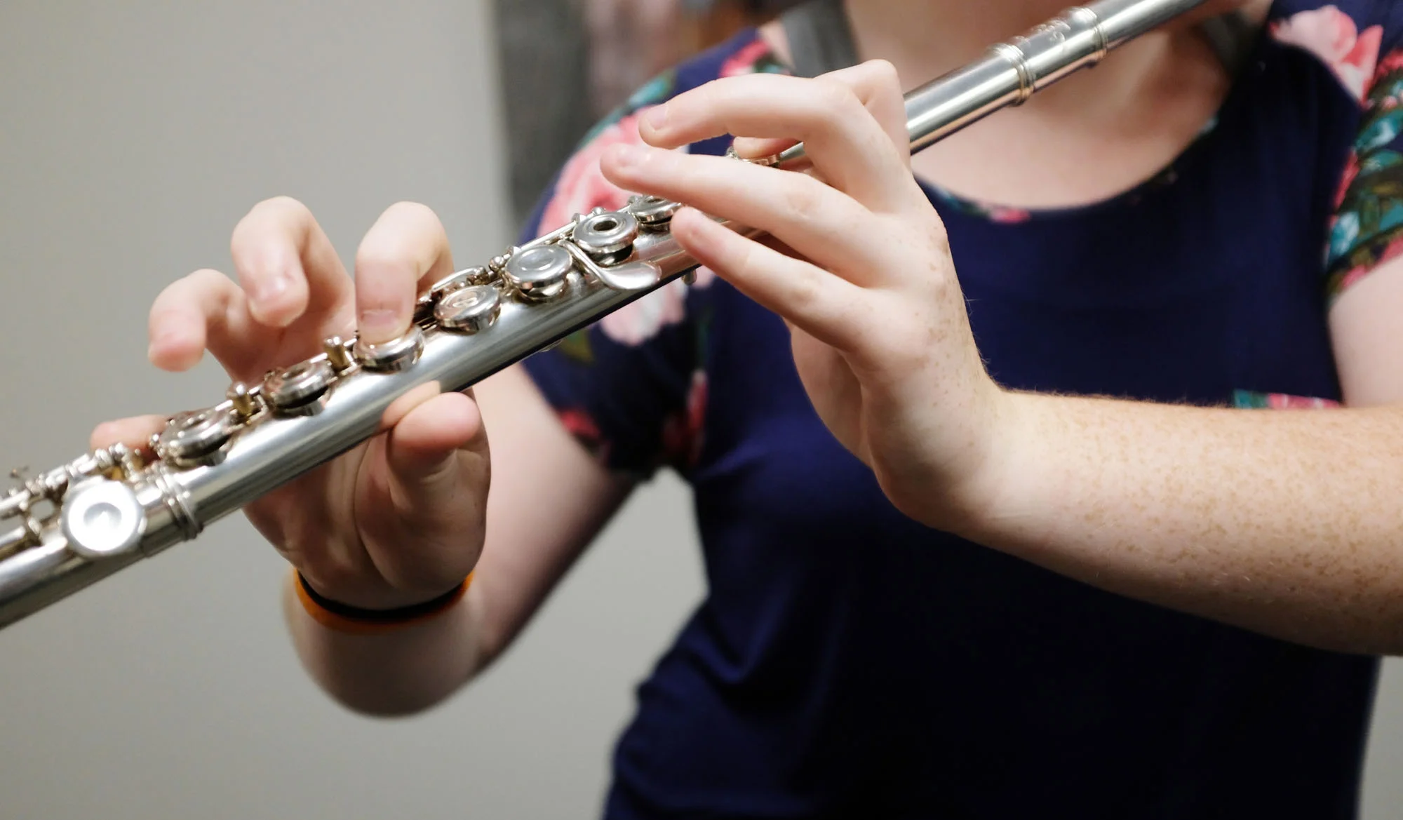 Close-up of a person playing a silver flute, with focus on their hands and the instrument.
