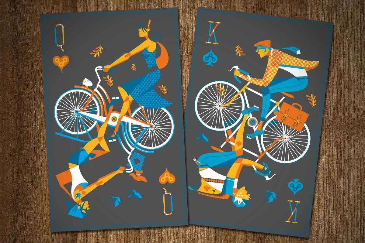 Two illustrated playing cards featuring people riding bicycles, set on a wooden surface. The left card depicts a woman in a blue dress with long hair, riding a bicycle, surrounded by autumn leaves, hearts, and clubs symbols. The right card shows a ma