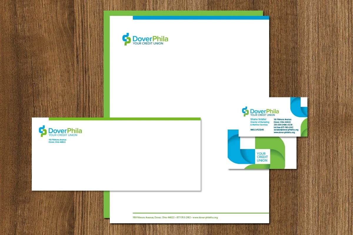Business stationery set for Dover Phila credit union, including letterhead, envelope, and business card, on a wooden surface. The design features the company's logo in blue and green, with contact information and a modern, professional layout.