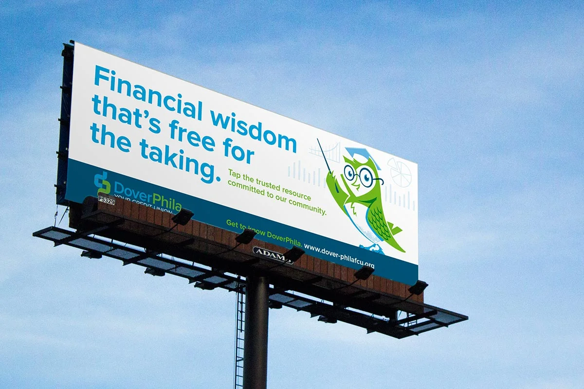 Billboard with message about financial wisdom and community resource, featuring a cartoon fish wearing glasses and a graduation cap, holding a fishing pole, set against a partly cloudy sky.