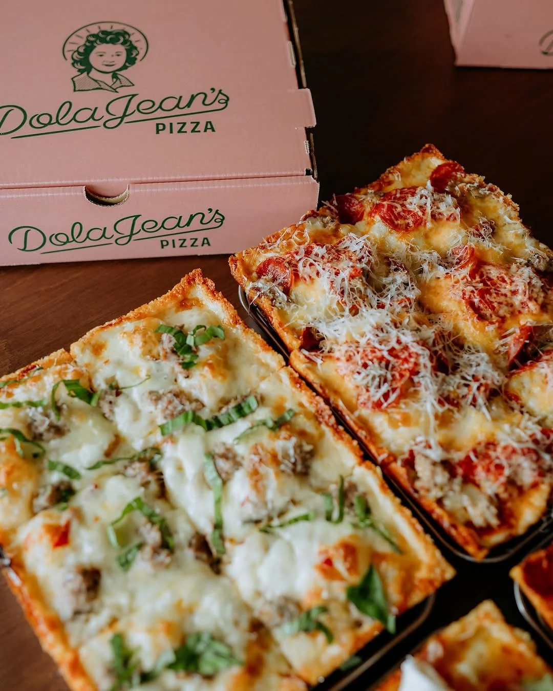 Two square slices of pizza with melted cheese, green onions, and ground meat, placed in front of a pizza box from Dolce Jean's Pizza.