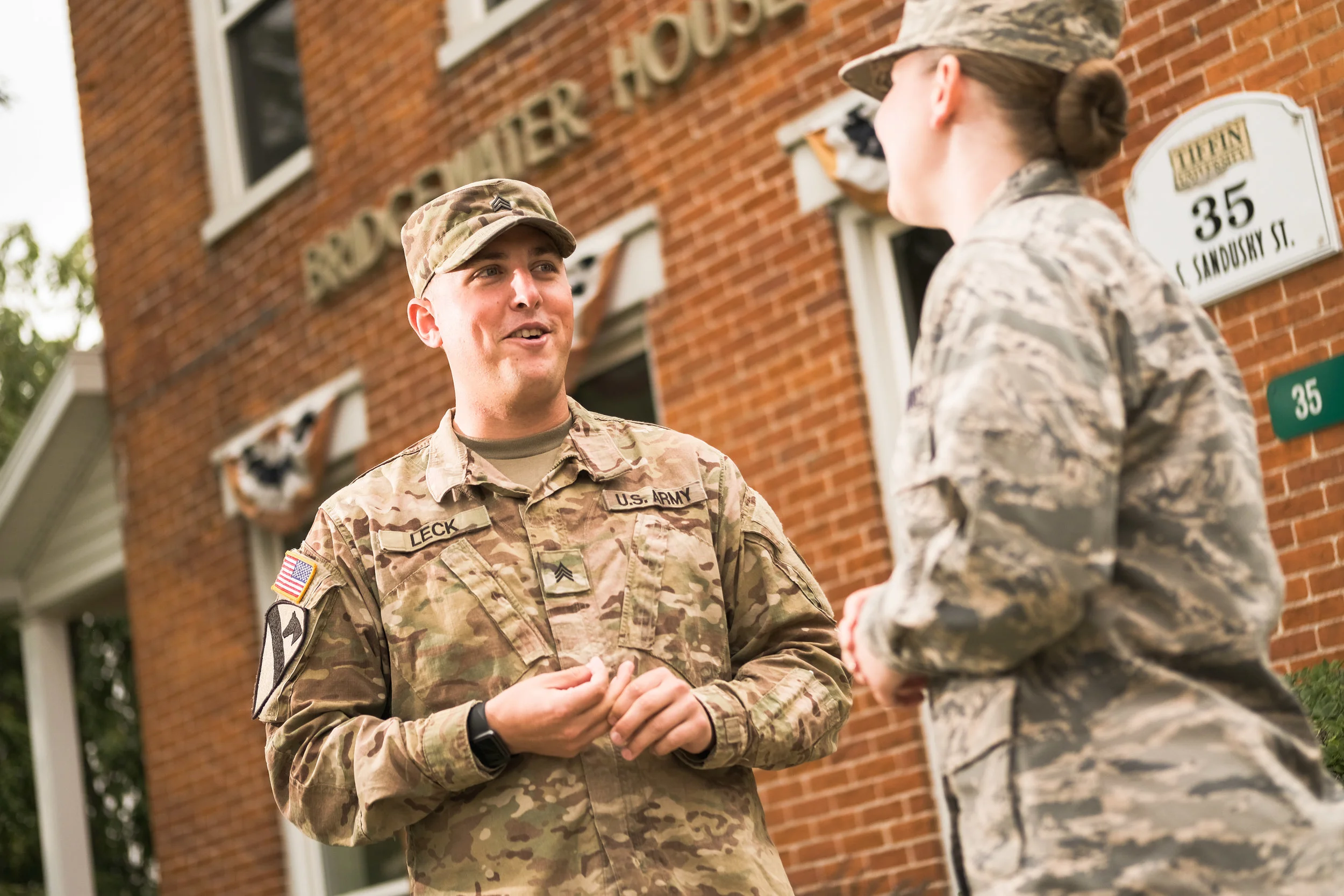 Two soldiers in uniform talking in front of a brick building decorated with patriotic bunting