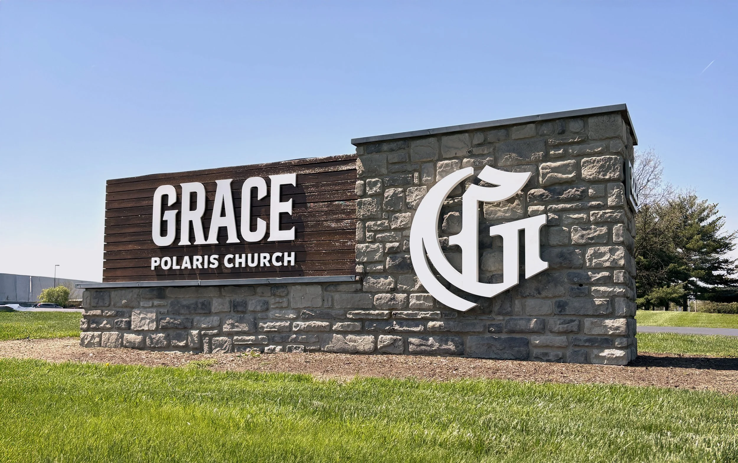 Sign for Grace Polaris Church, featuring the church's name in large white letters on a wooden background, with a logo combining the letters G and P in white on a stone wall.