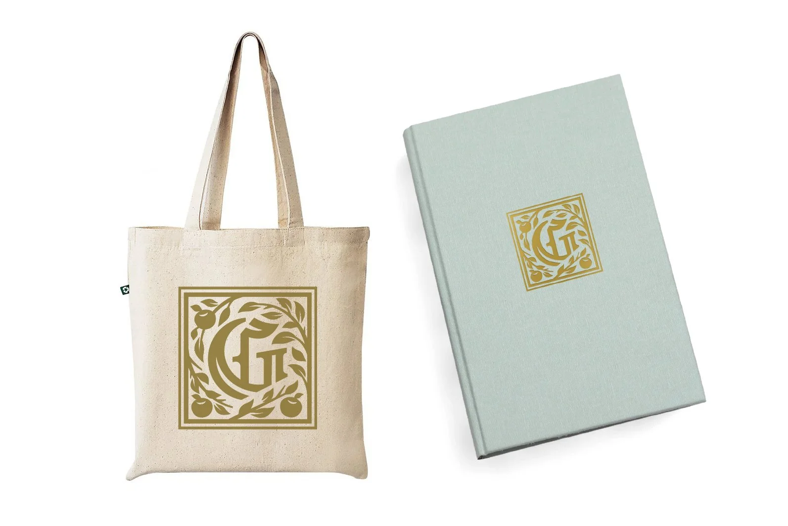 A beige tote bag and a light blue hardcover notebook or journal, both with a gold logo featuring the letter G surrounded by decorative foliage.