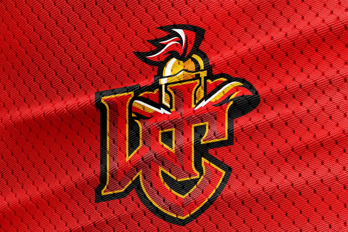 Close-up of a sports team logo embroidered on red mesh fabric, featuring a stylized letter 'L' with the words 'Los Angeles' integrated into a crest, topped with a cartoonish eye and a red, black, and yellow color scheme.