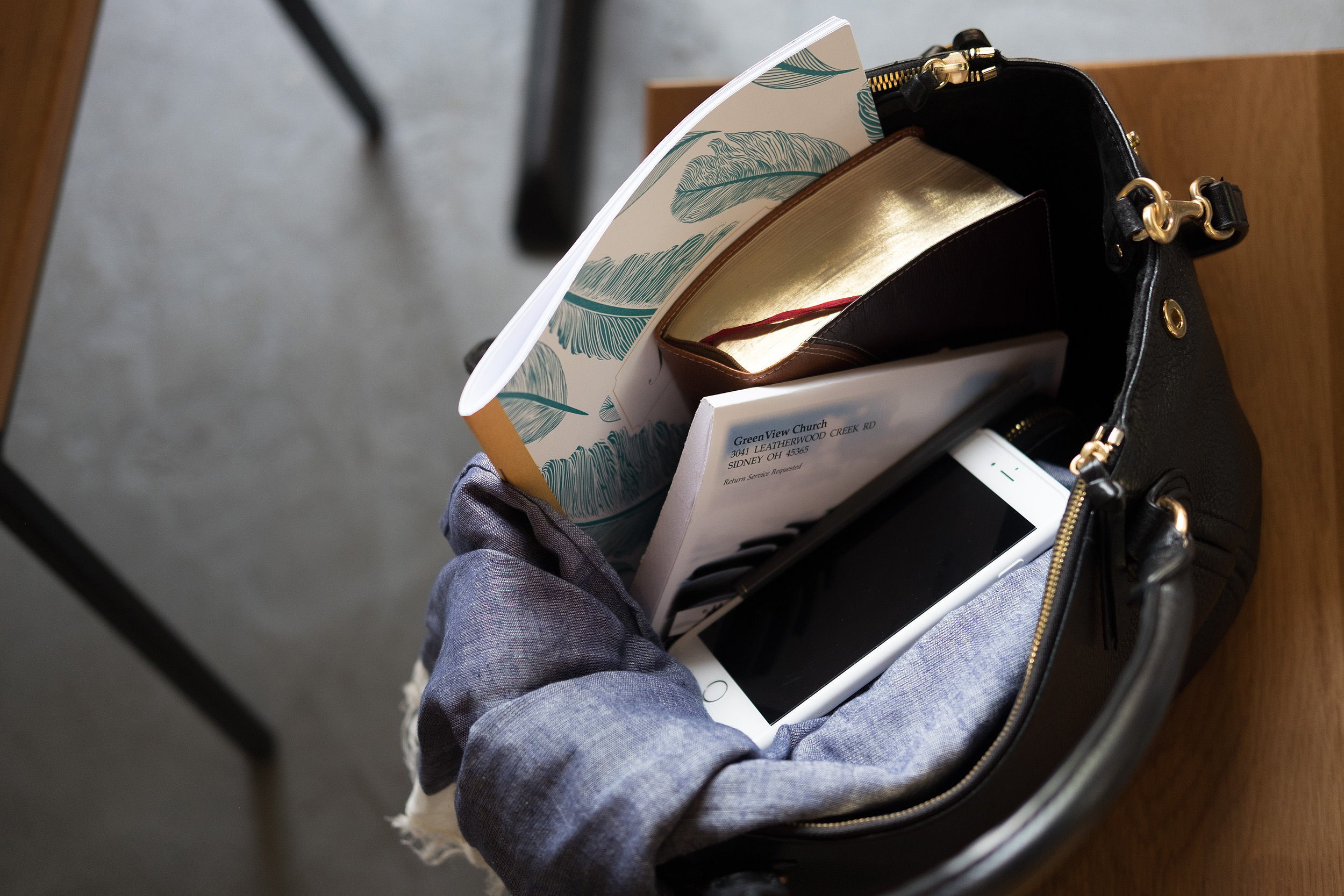 Black handbag on a wooden table with books, a smartphone, and a scarf inside.