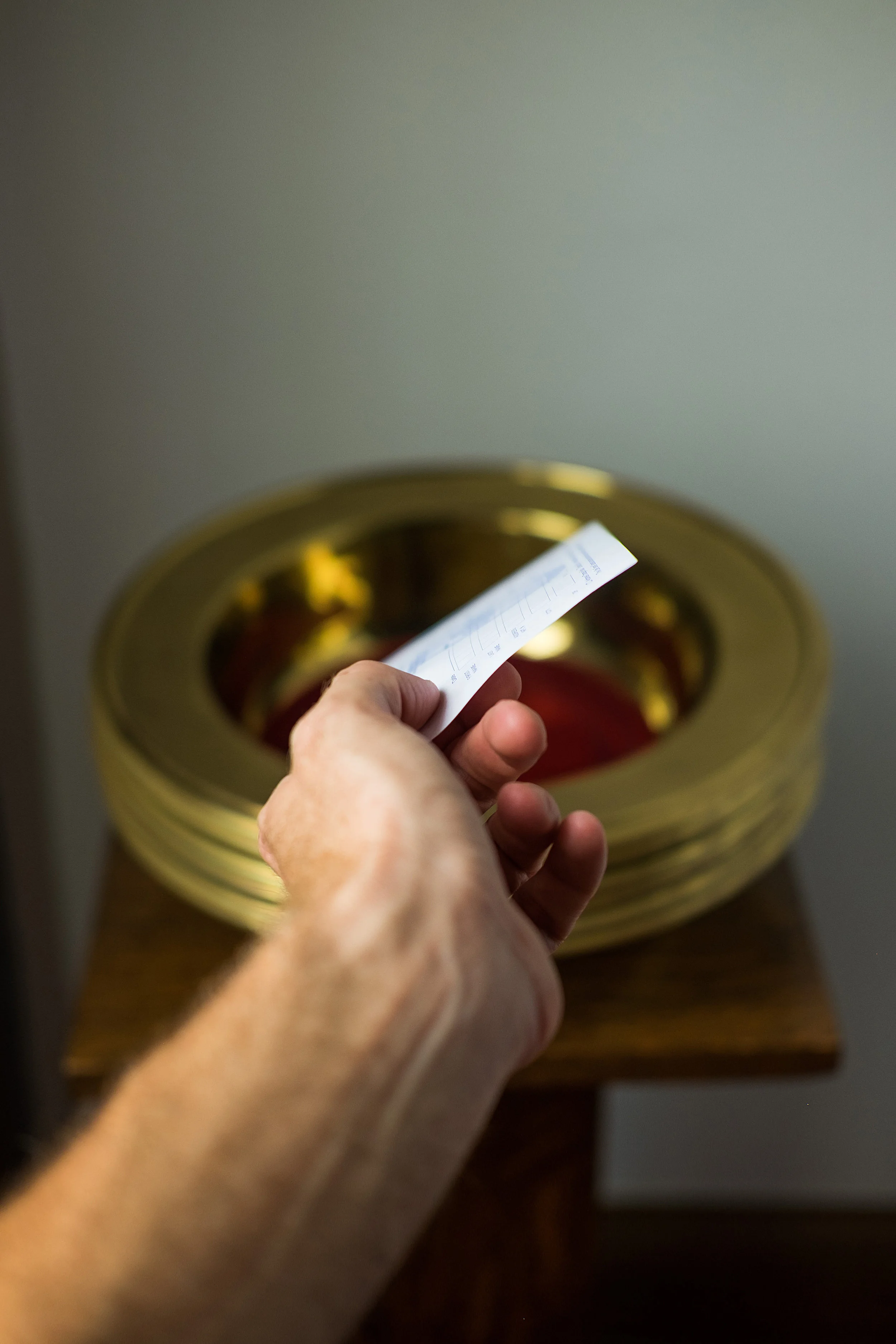 A hand holds a thermostat or temperature sensor in front of a stack of gold-colored lids or trays on a wooden surface.