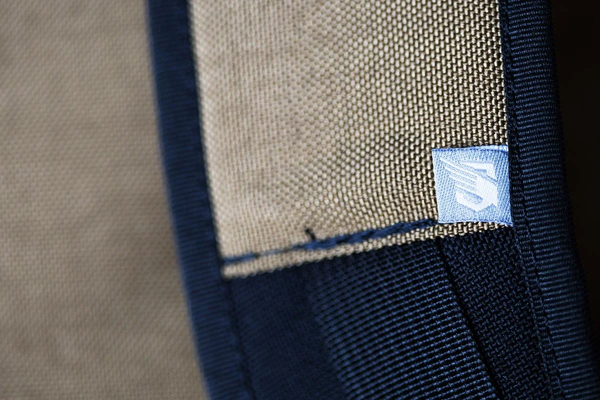 Close-up of a fabric pocket with a beige mesh material and a navy border, featuring a small blue and white label.