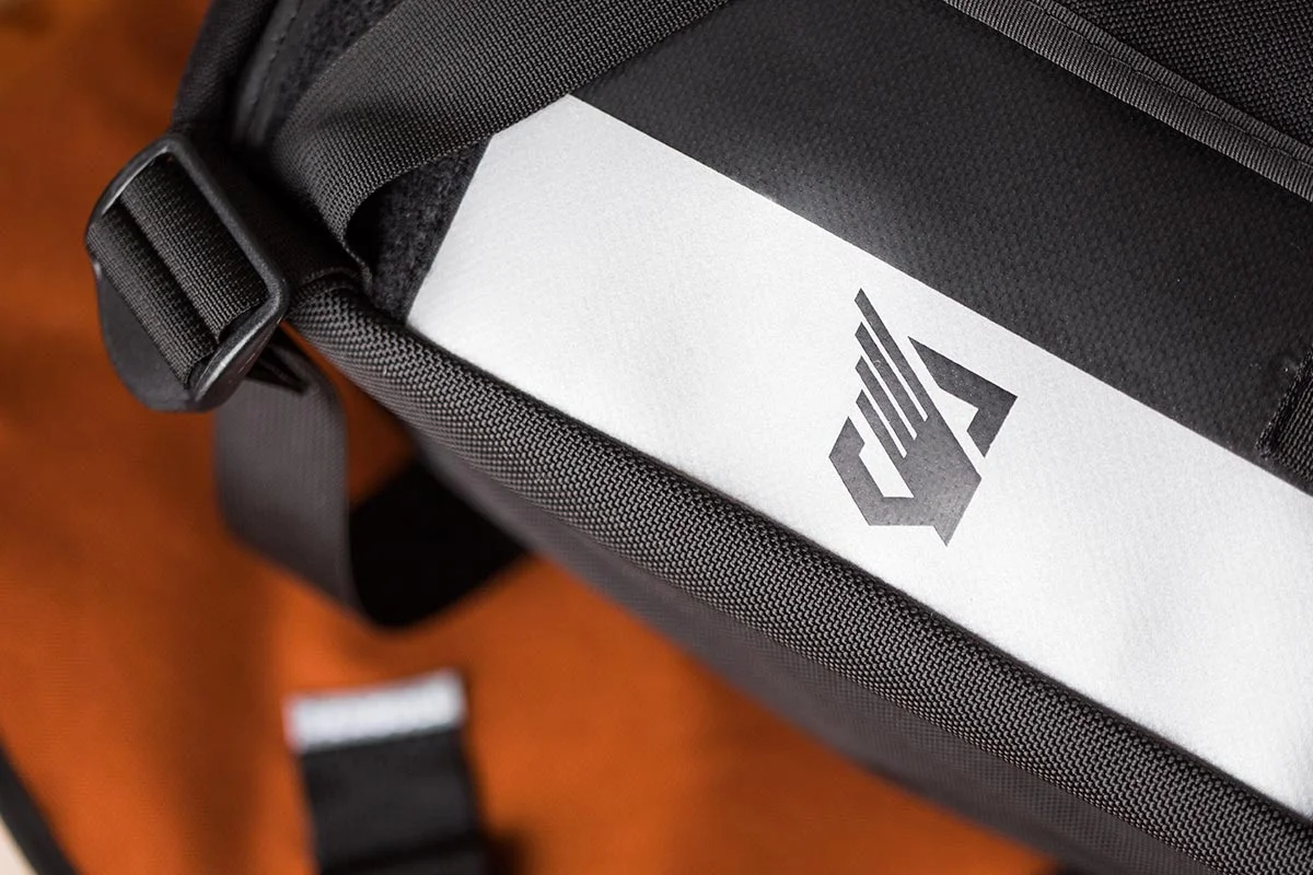 Close-up of a black carry bag with a white folder inside, showing a logo of a mountain peak with a stylized letter A on it.
