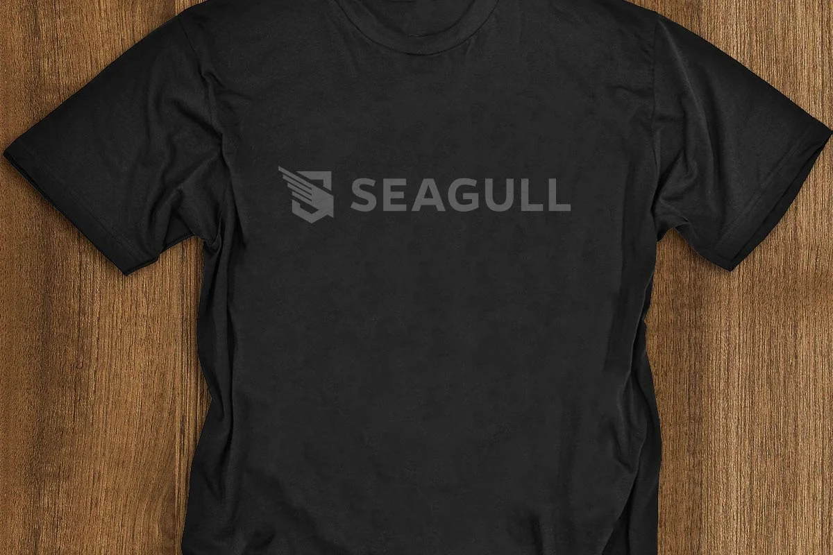 Black T-shirt with the logo and name 'SEAGULL' printed on the front, laid flat on a wooden surface.