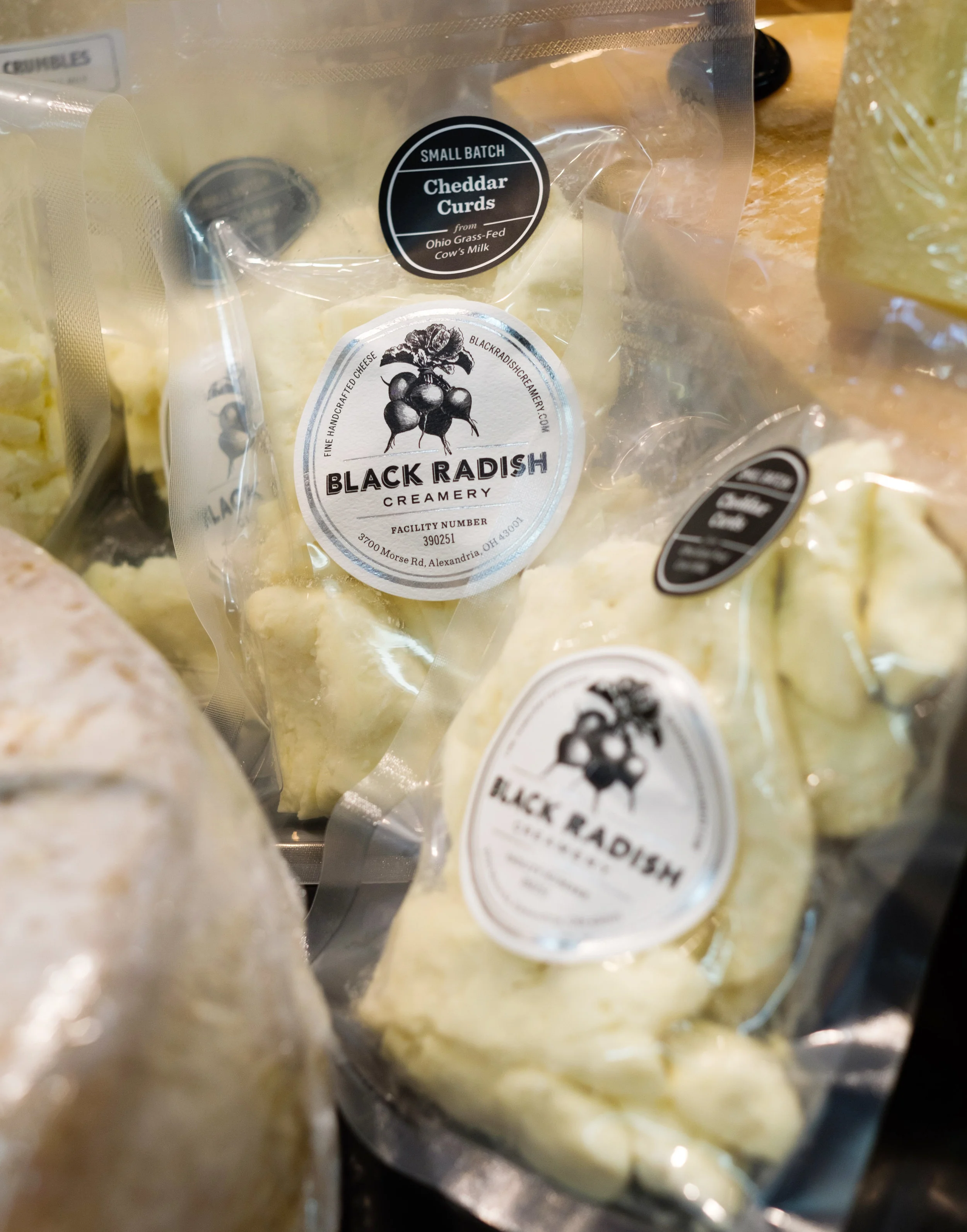 Packages of Black Radish Creamery cheddar curds from Ohio Grass-Fed Cow's Milk in clear plastic bags with black and white labels.