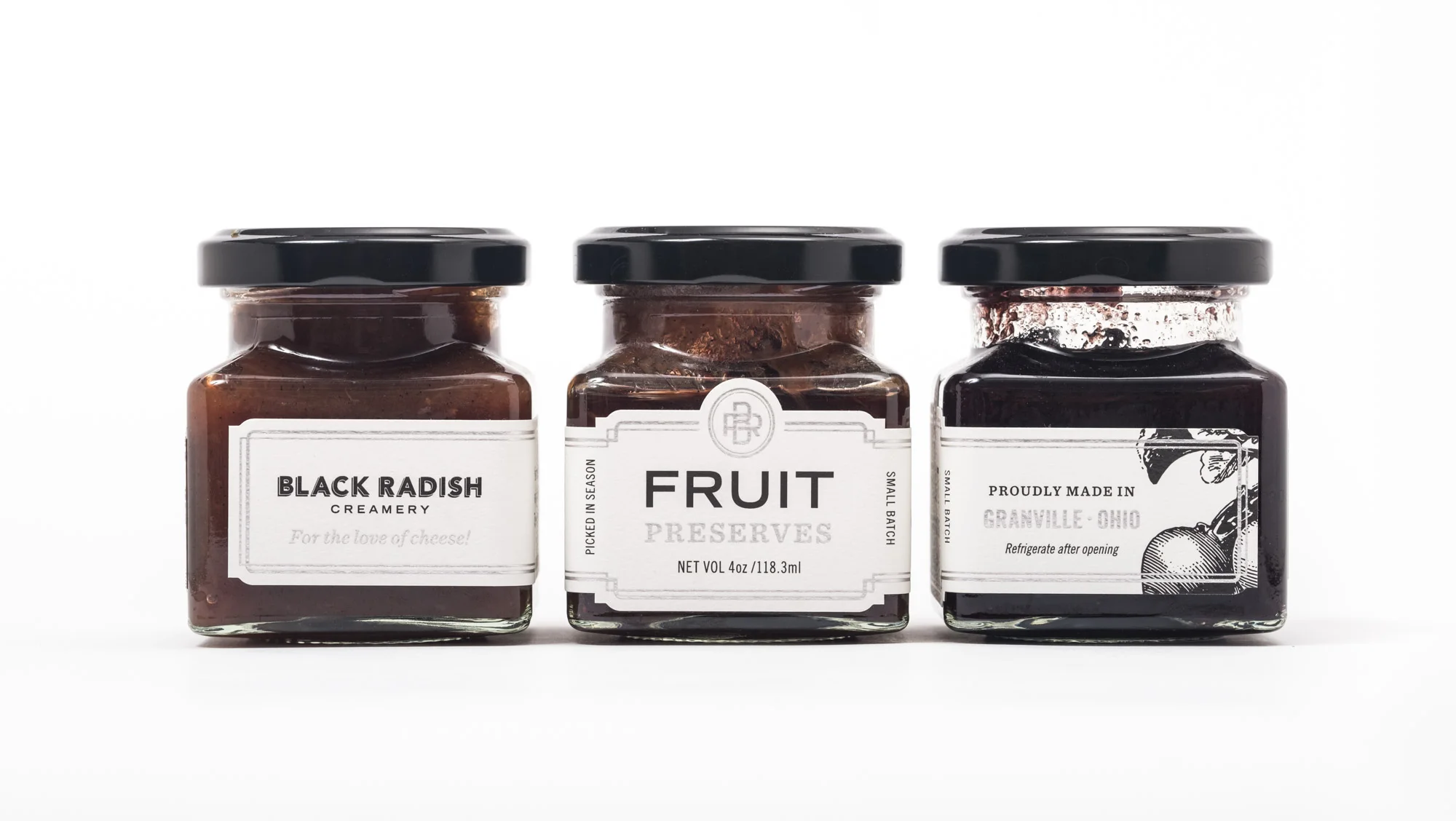 Three jars of preserves and spreads with black lids, labeled 'Black Radish Creamery,' 'Fruit Preserves,' and 'Proudly Made in Granville Ohio,' on a white background.