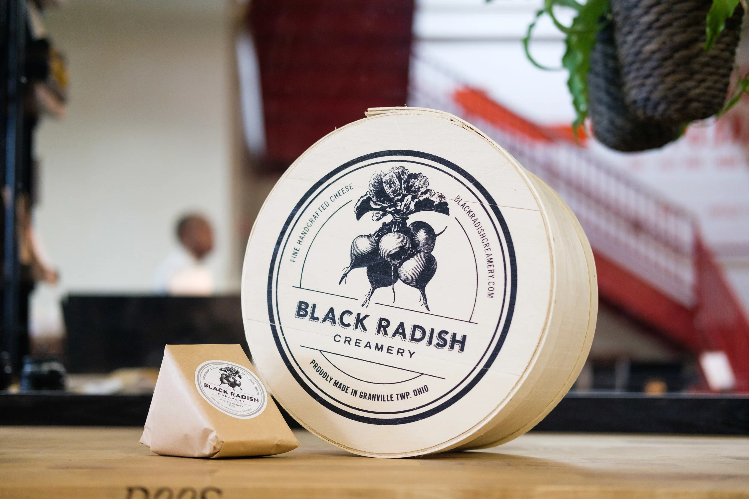A large round container with a vintage label for Black Radish Creamery, featuring an illustration of radishes and the text 'Black Radish Creamery' and 'Proudly made in Granville, Ohio.' Next to it is a smaller wrapped package with similar branding. I