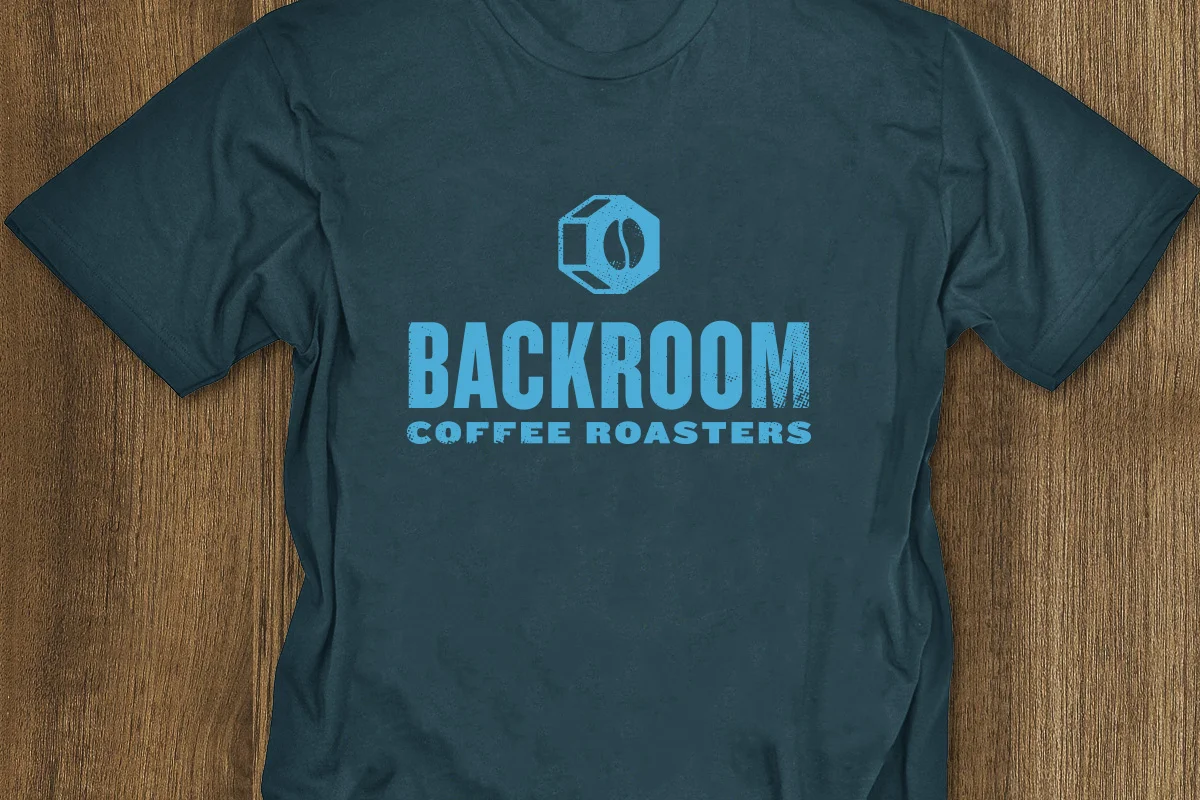 Gray T-shirt with a blue logo featuring a coffee bean and a coffee container, and text that reads 'BACKROOM Coffee Roasters' in bold and smaller font.